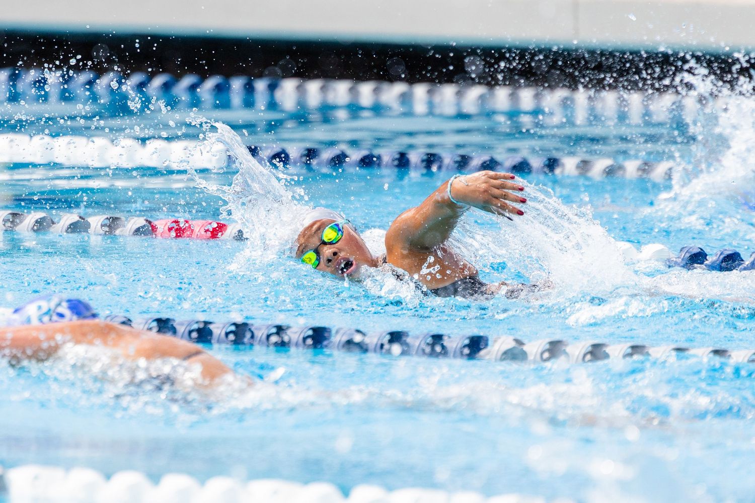 Competitive swimmer doing freestyle stroke in outdoor pool lane wearing colorful goggles and swim cap.