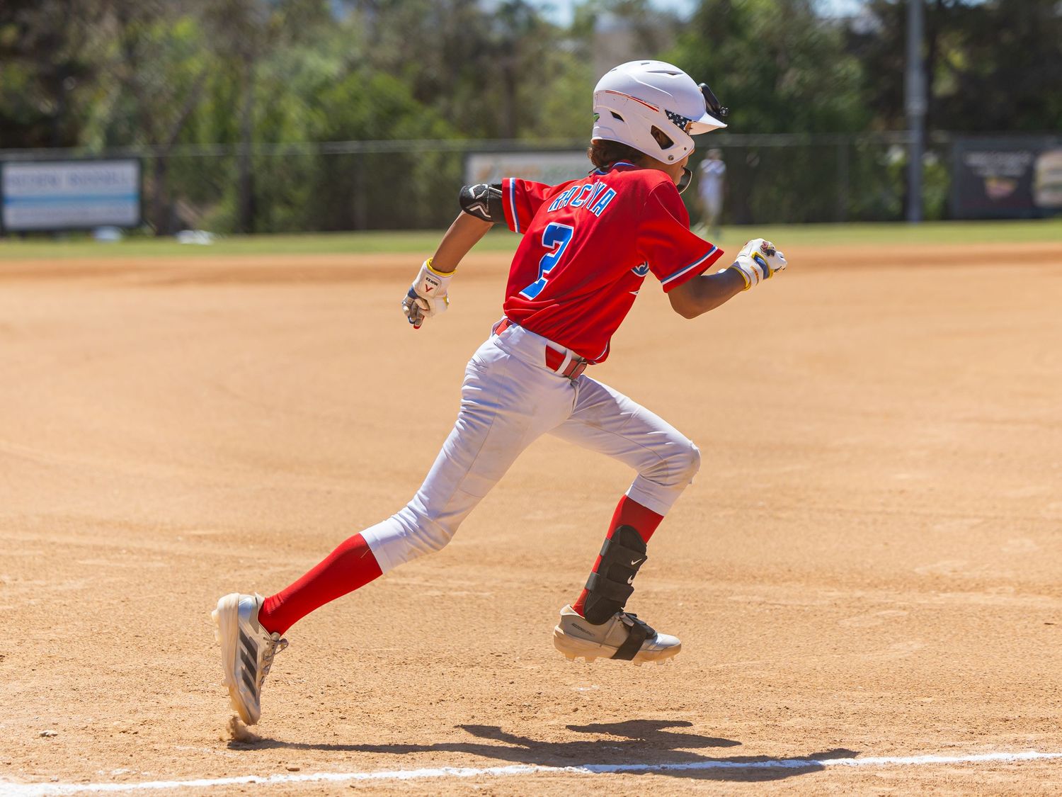 Baseball player in red uniform sprints down baseline during youth baseball game.