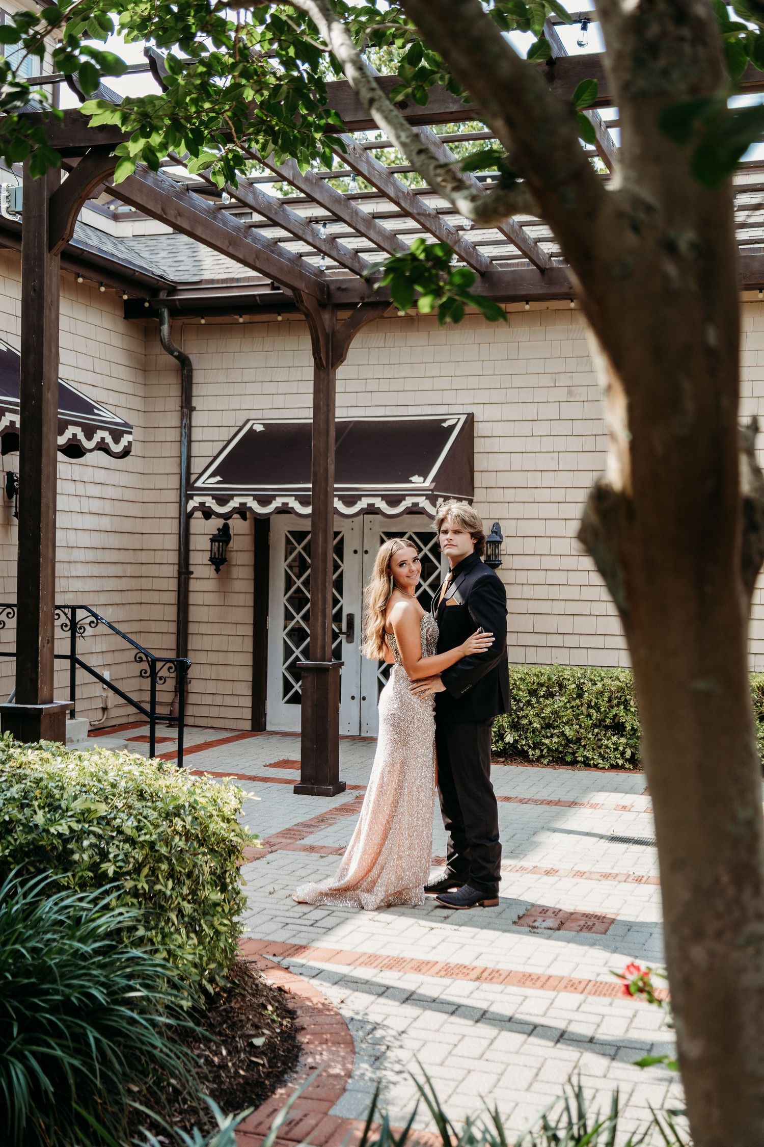 A couple shares a romantic moment under a pergola in a garden courtyard.