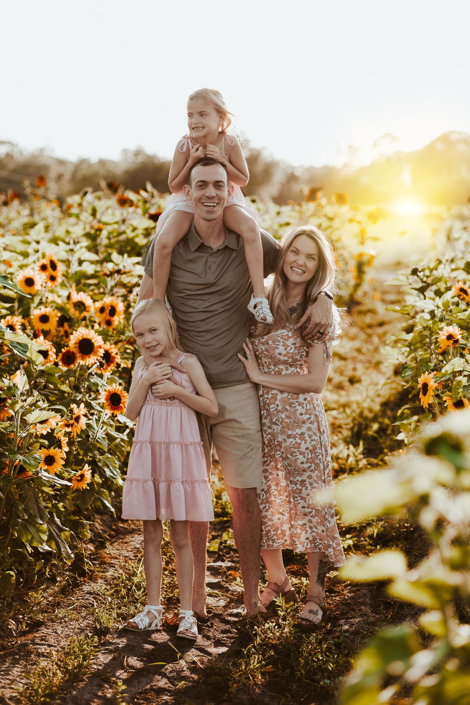 A family poses together in a sunflower field during sunset.