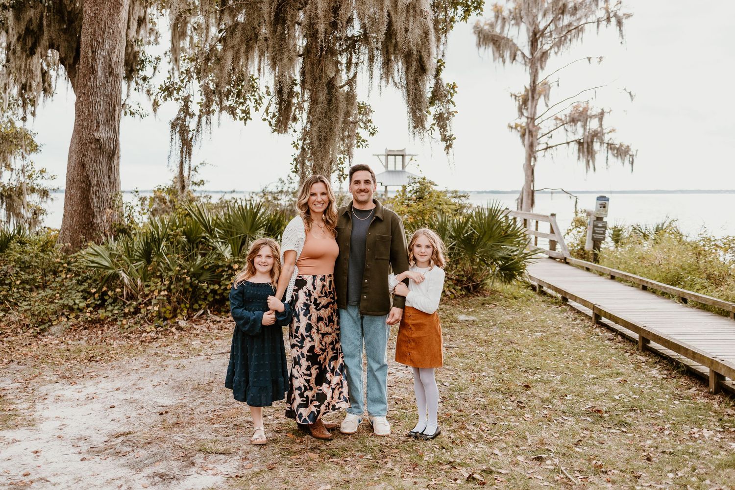 A group stands together on a path under Spanish moss-draped trees beside a coastal waterway.