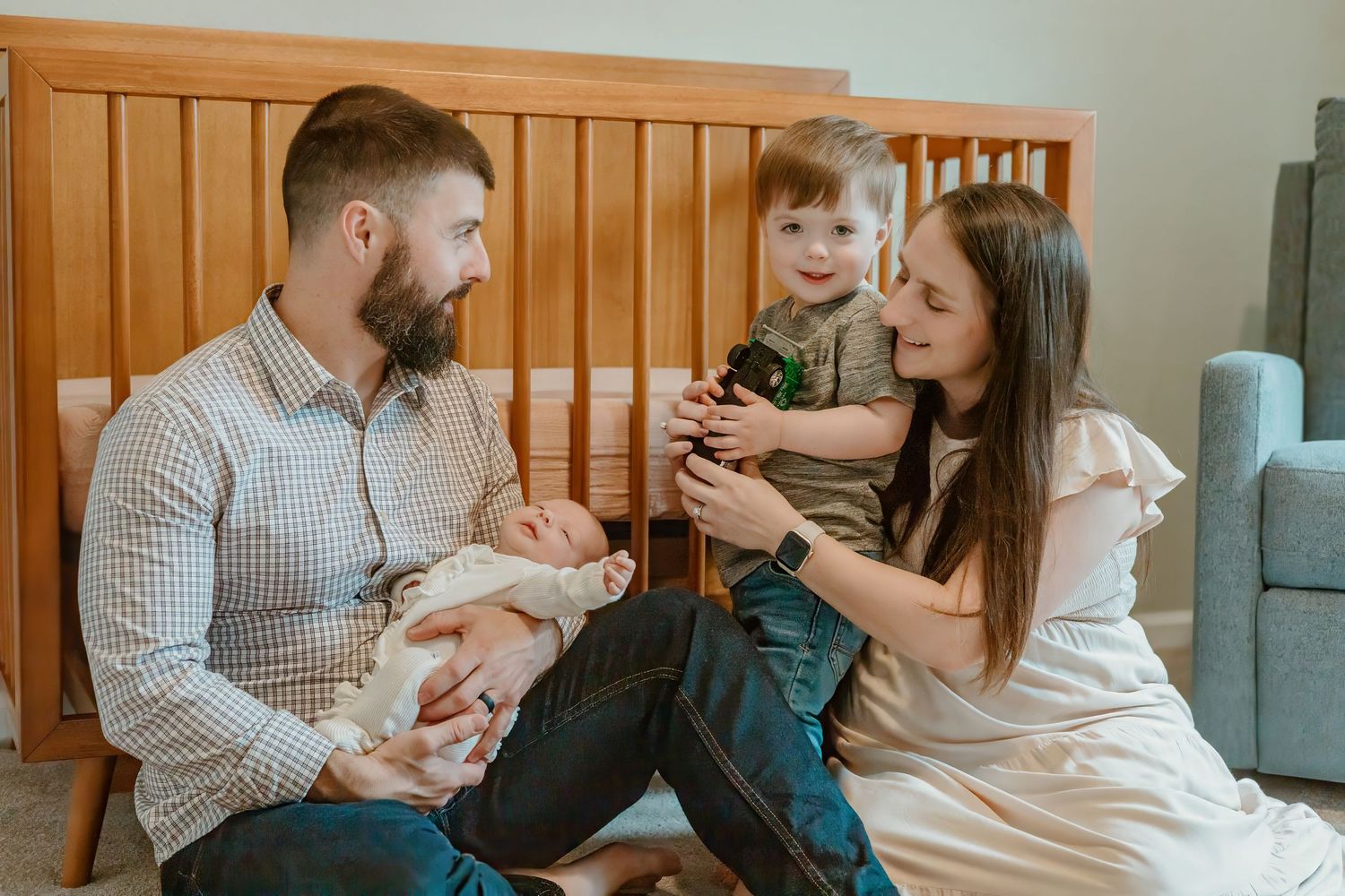 A family relaxes together on a couch with wooden paneling visible in the background.