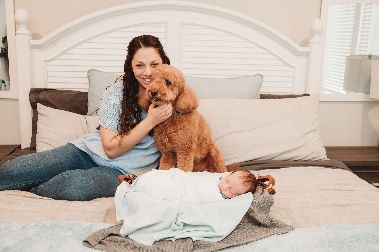 Family relaxing on bed with their goldendoodle dog and newborn baby.
