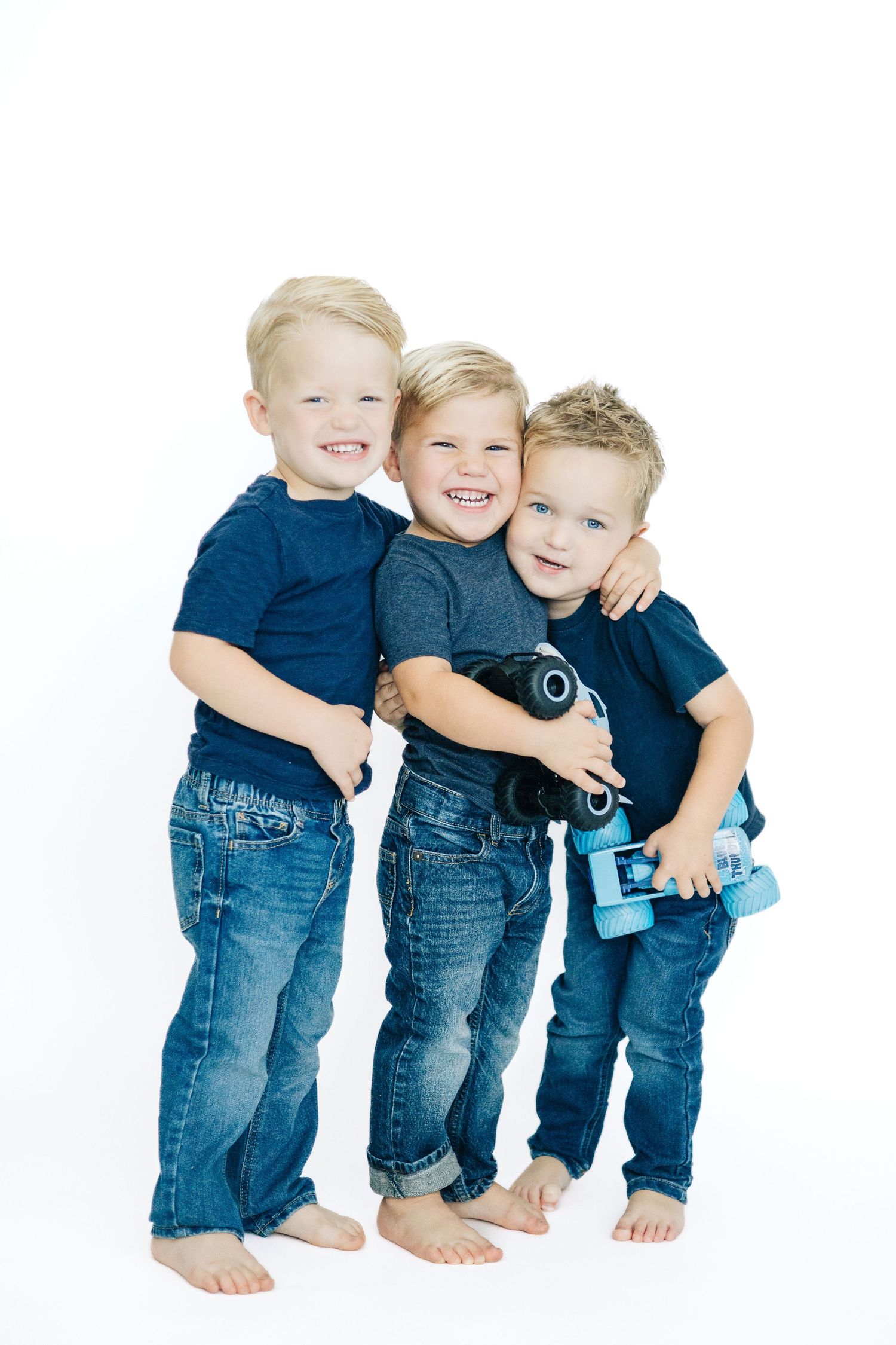 Three young children in matching blue jeans and t-shirts playing together against a white background.