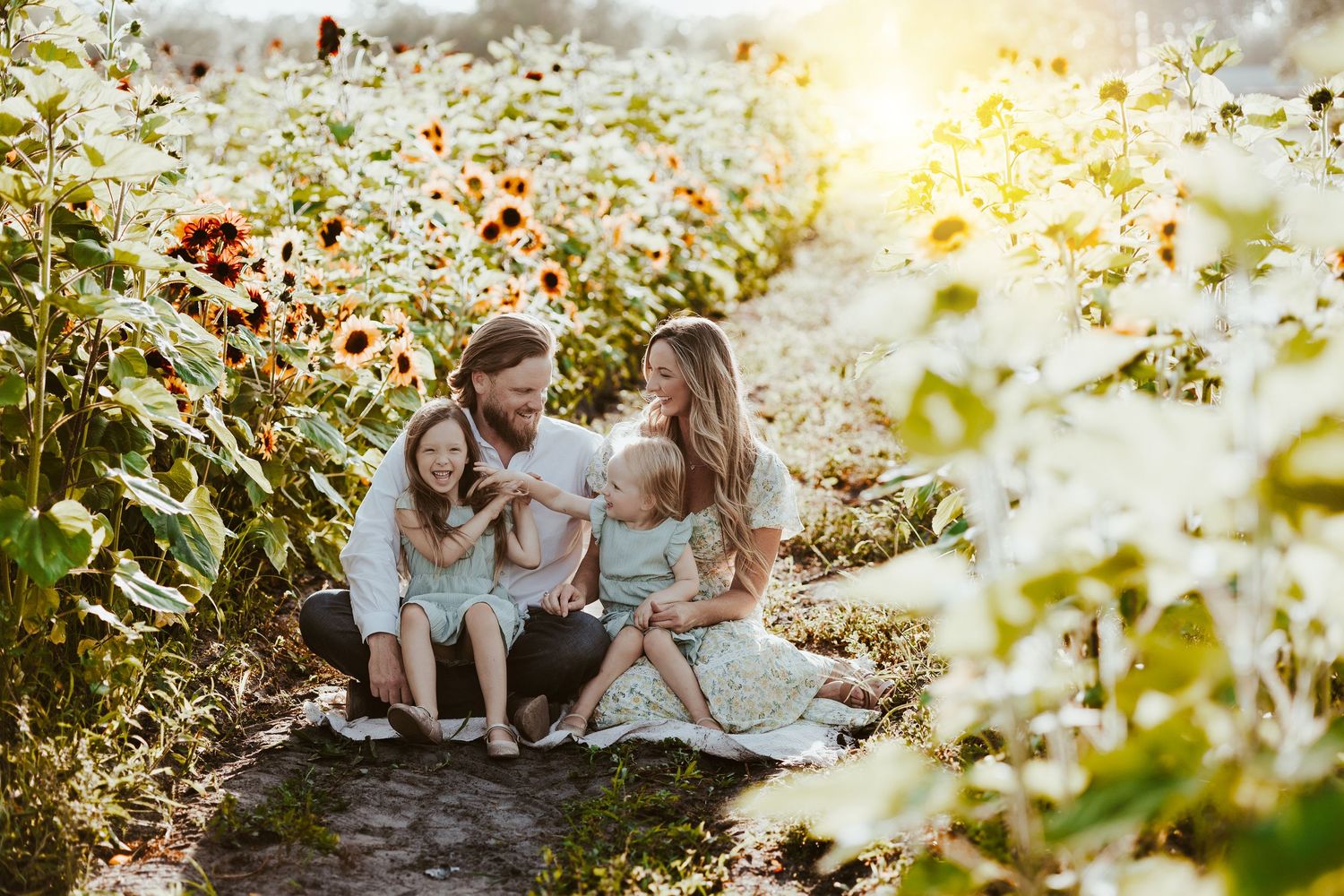 Family sitting together in a sunlit garden with white flowers and greenery during golden hour.