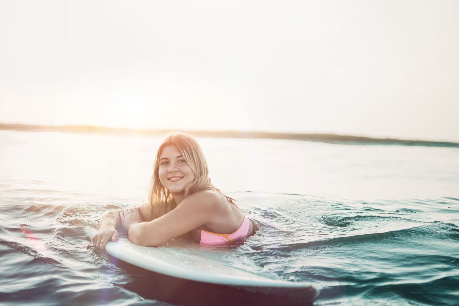 Person enjoying a summer day paddleboarding on calm waters during sunset.