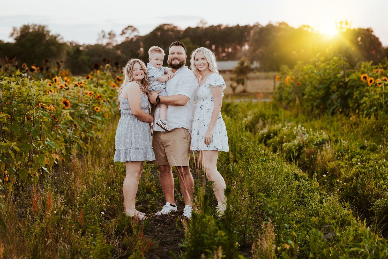 Family portrait session in golden sunflower field during sunset.