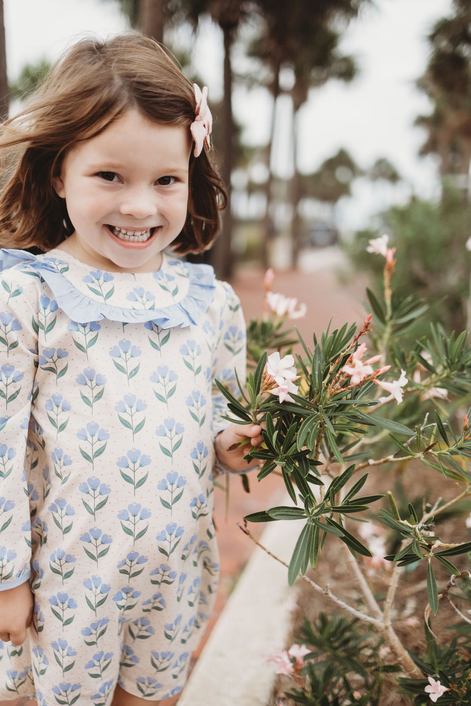 Three photos showing a child in a white and blue floral dress exploring outdoor plants and flowers in a garden setting.