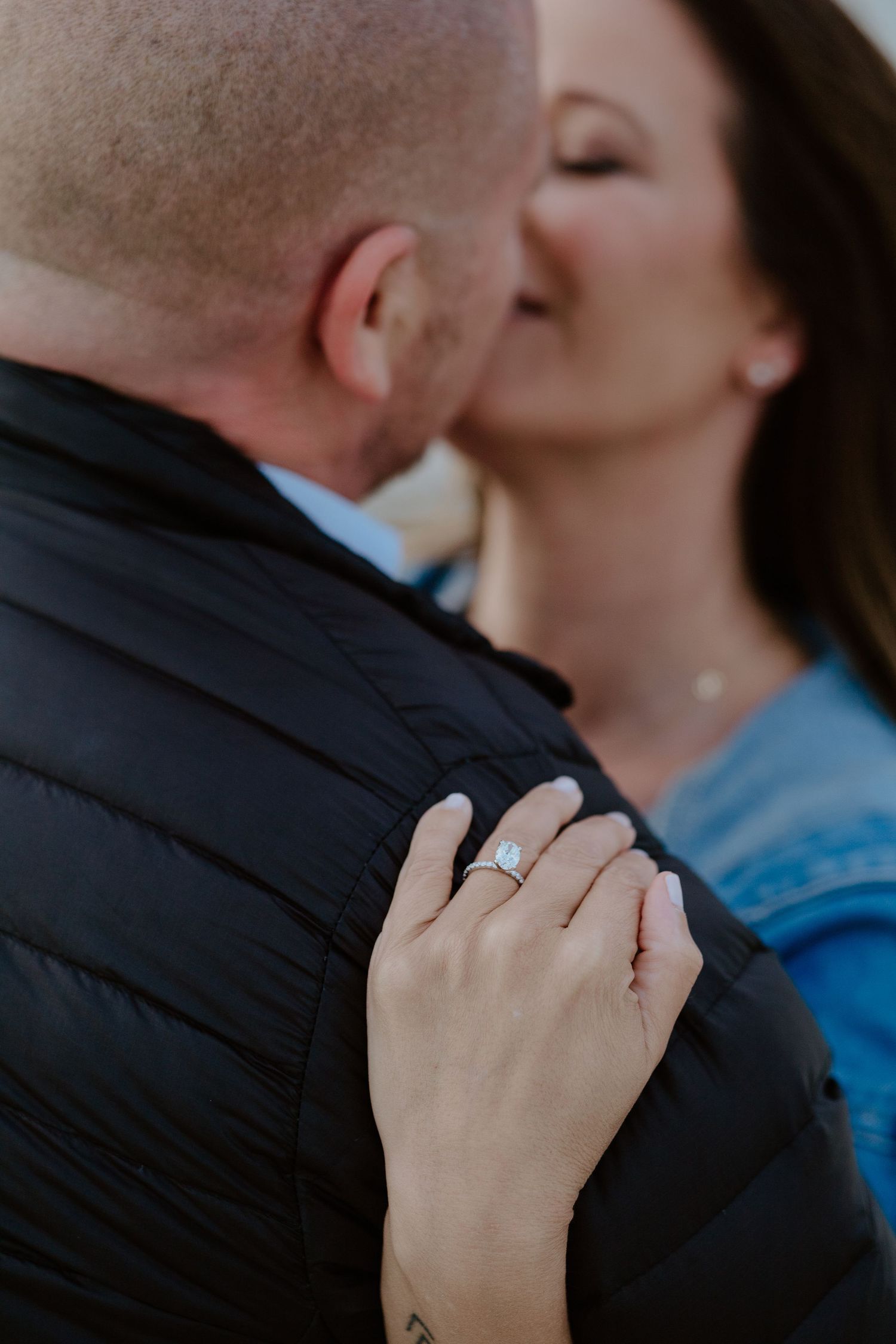 A close-up view of an engagement ring on a woman's hand as a couple embraces in a romantic moment.