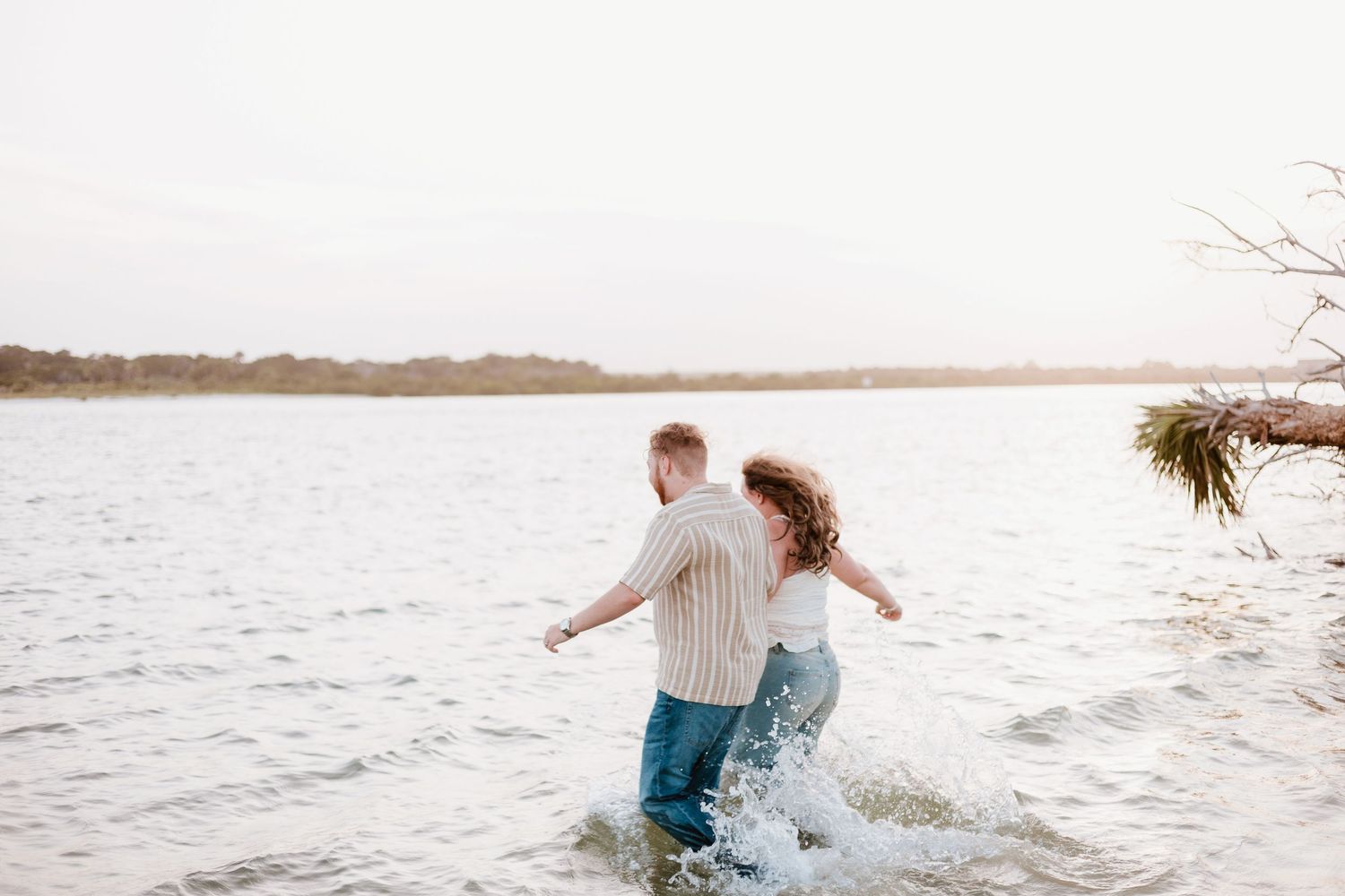 Two people splash and play in the ocean waves at sunset.