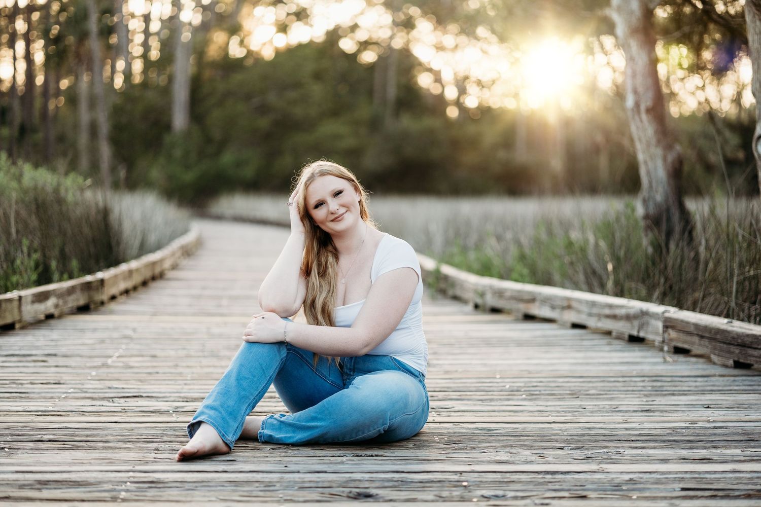 Person in casual attire posing on wooden boardwalk at sunset.