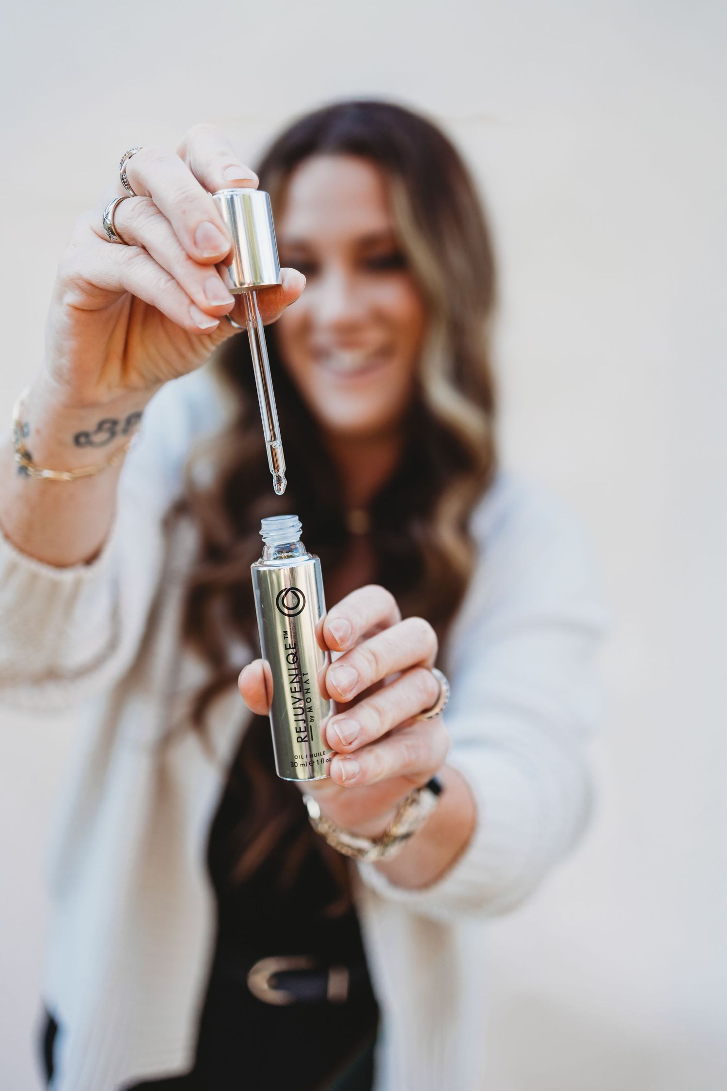 Hands holding and displaying a small glass vial with dropper containing CBD or essential oil product against white background.