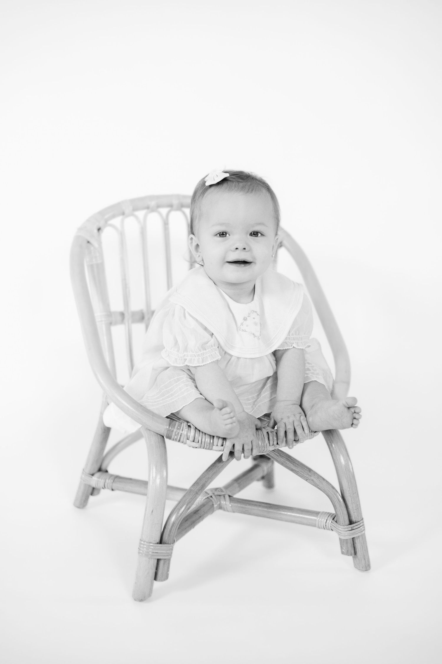 Baby sits in white wooden rocking chair during professional photo session.