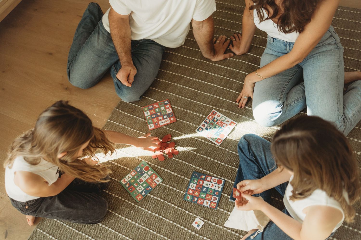 Friends sitting on a patterned rug playing a board game together in a cozy indoor setting.