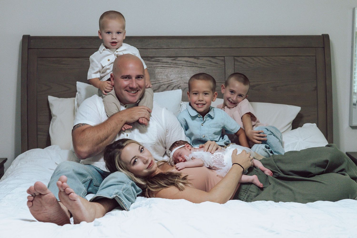 Family lounging together on gray bed during casual photo session.