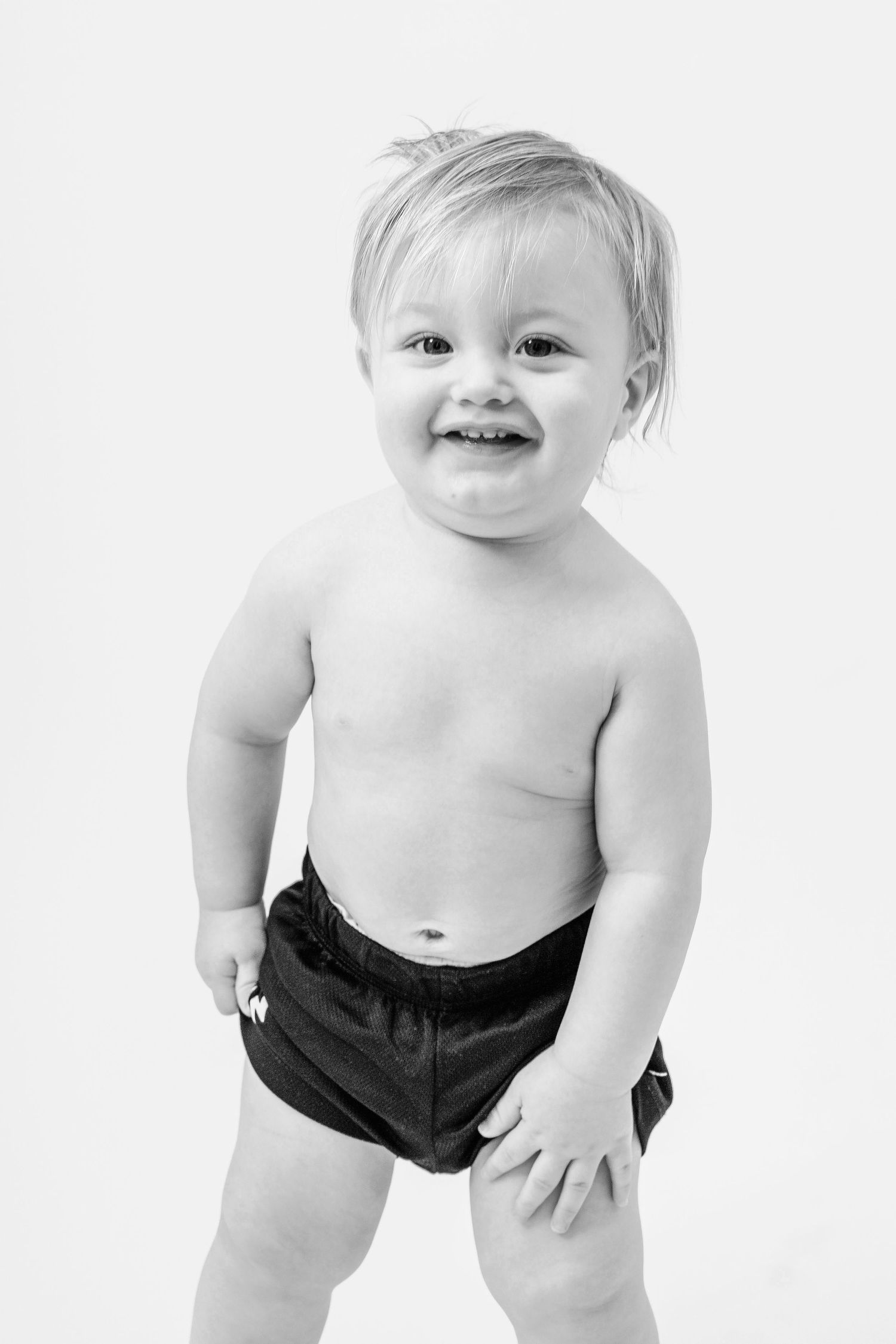 Joyful baby wearing black shorts crawls and smiles in a series of three connected photos on white background.