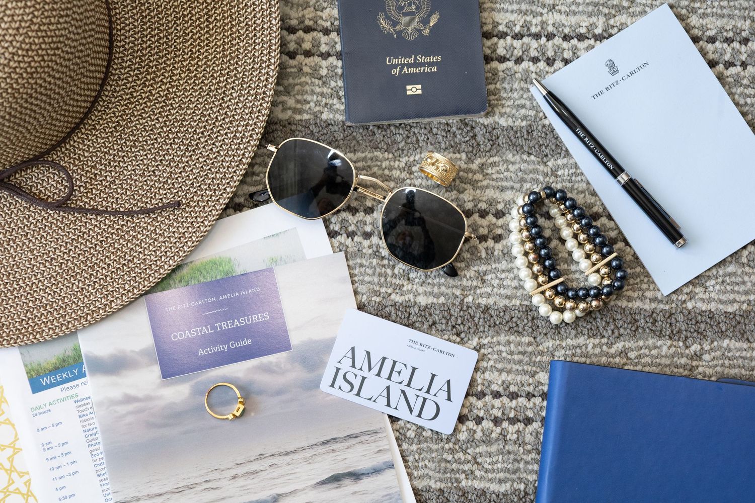 Travel essentials flatlay with passport, straw hat, and accessories on textured surface.