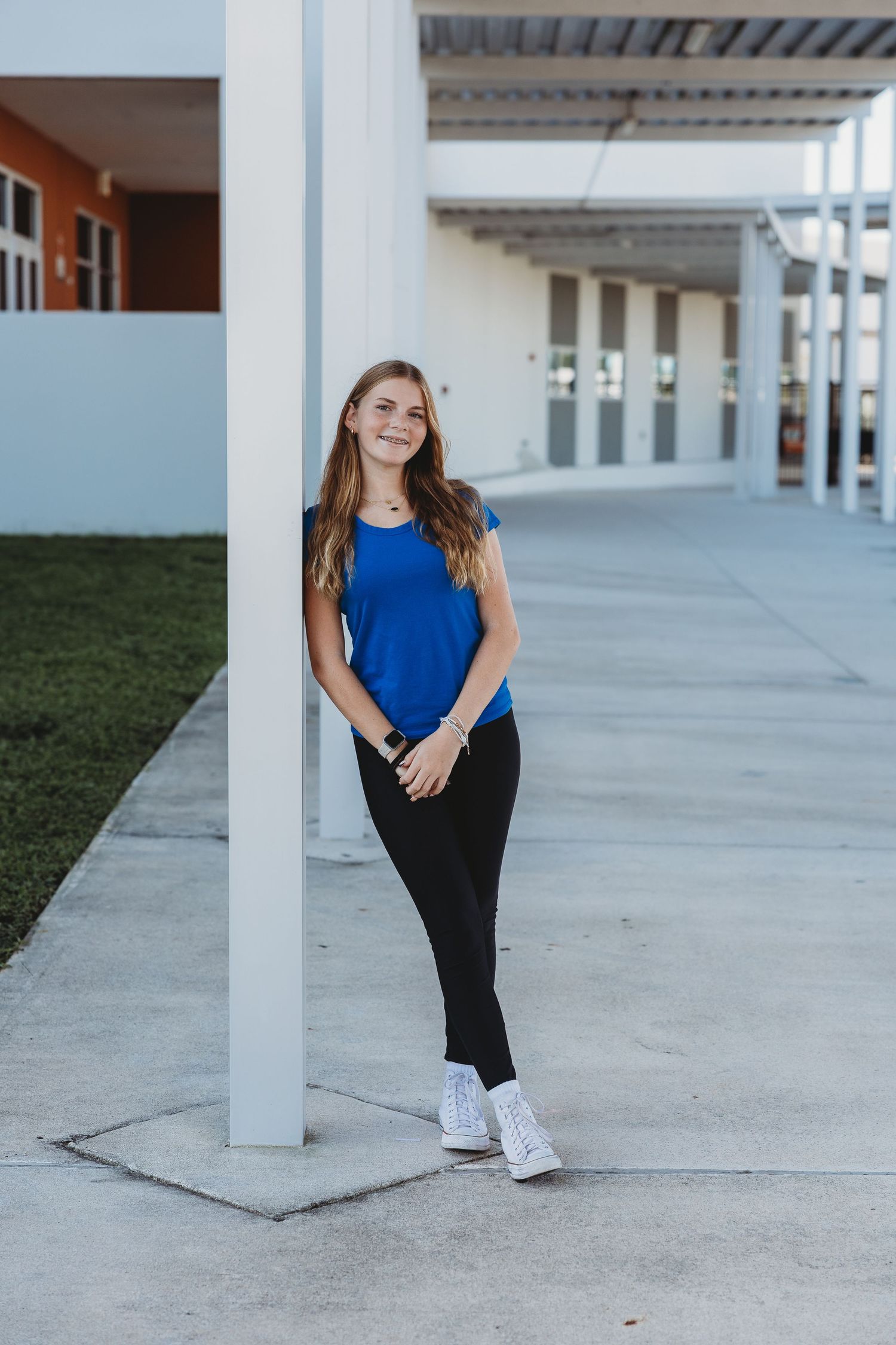 Person in blue top and black pants posing under covered walkway with columns.