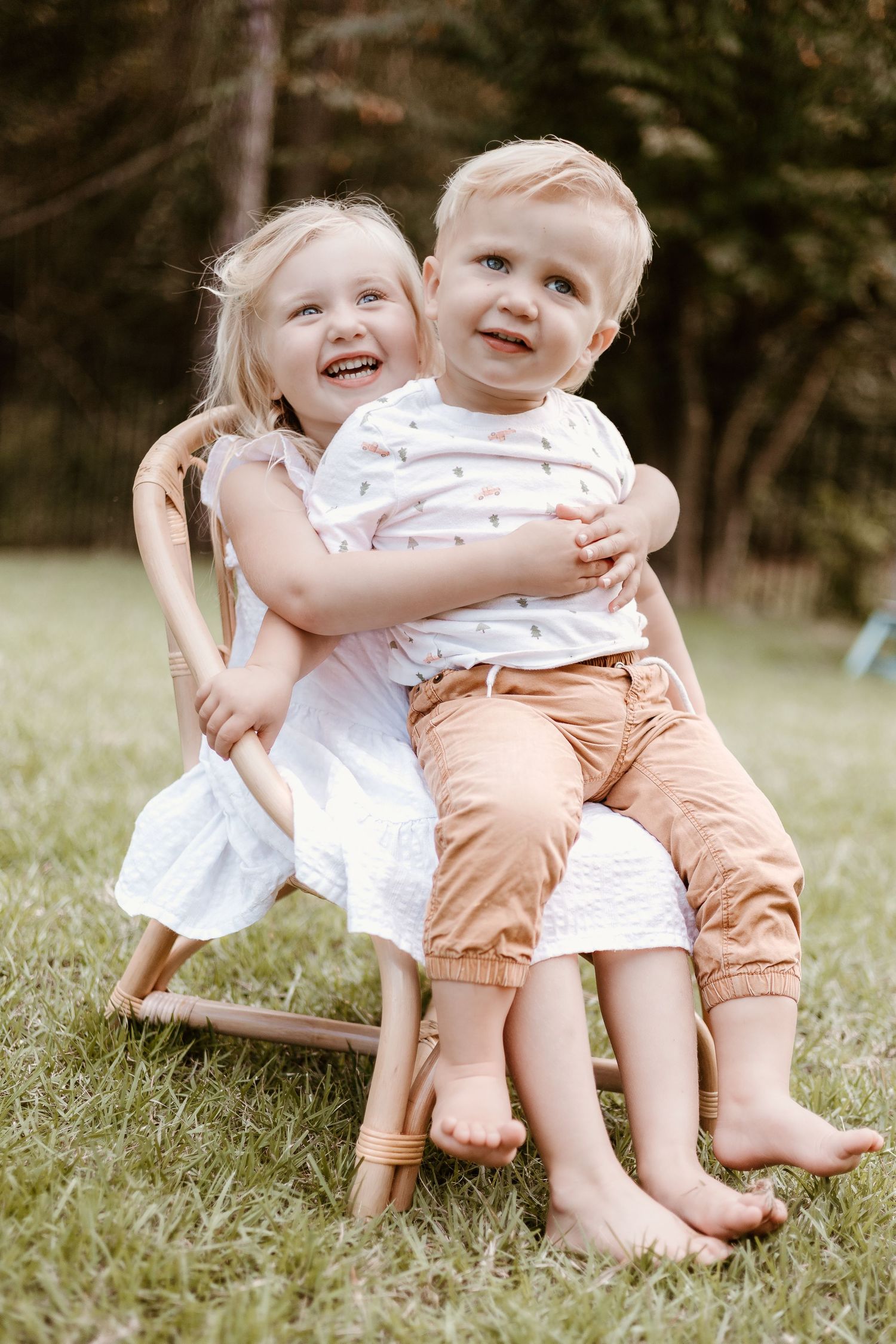 Two young children laughing together on wooden rocking chair outdoors.