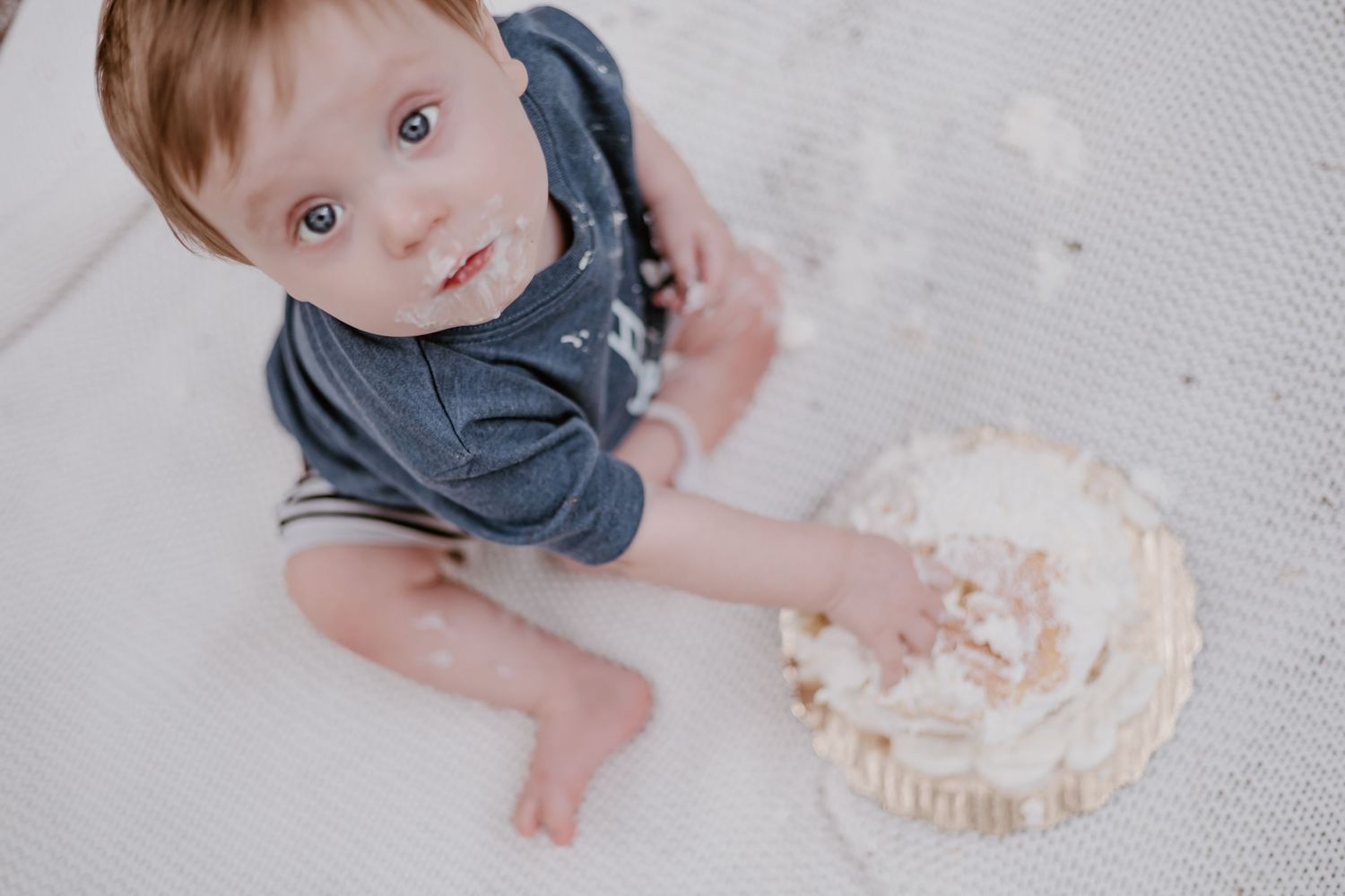 Baby's hands reaching for white frosted cake on textured surface.