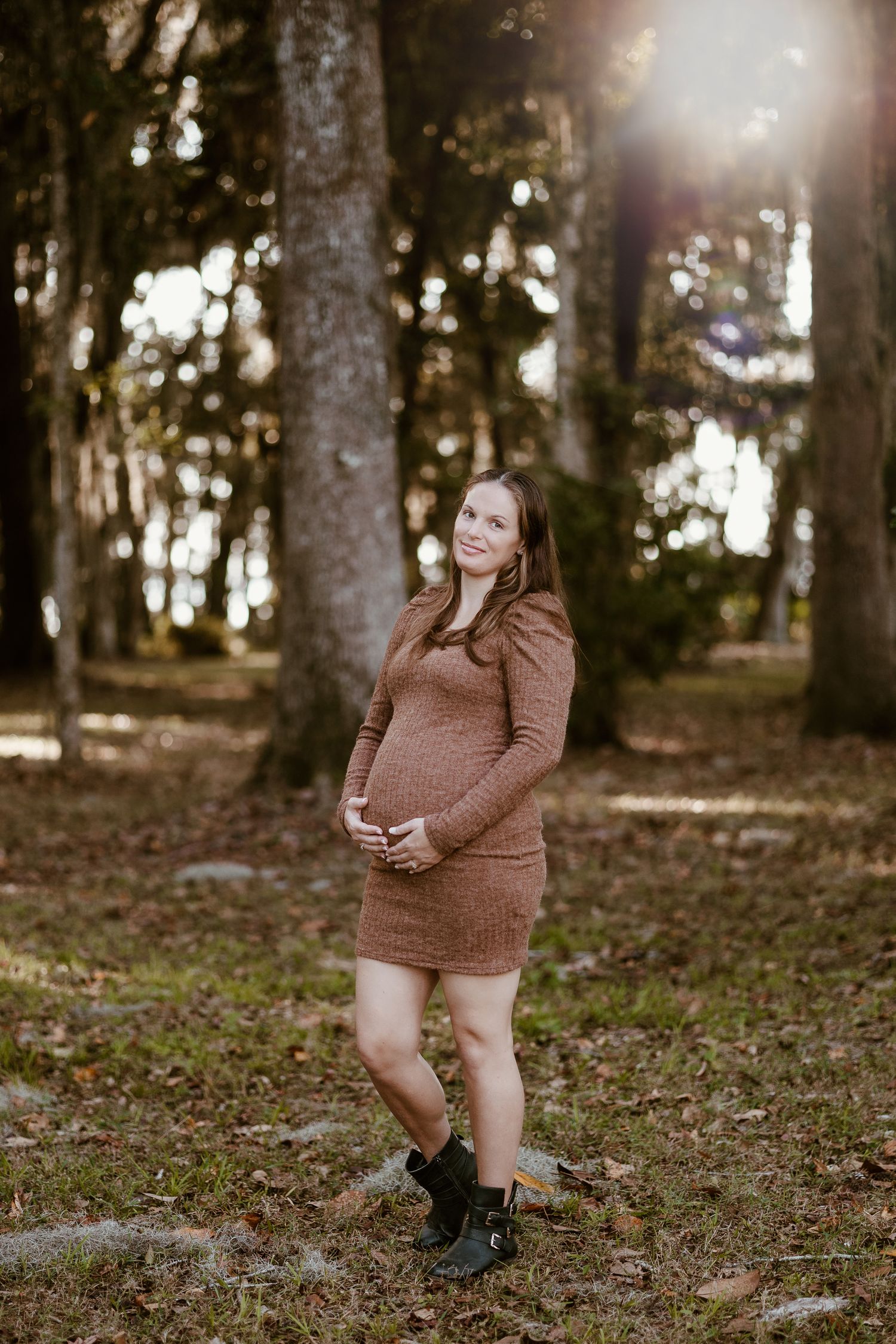 Maternity photography session captured in a sunlit forest setting.