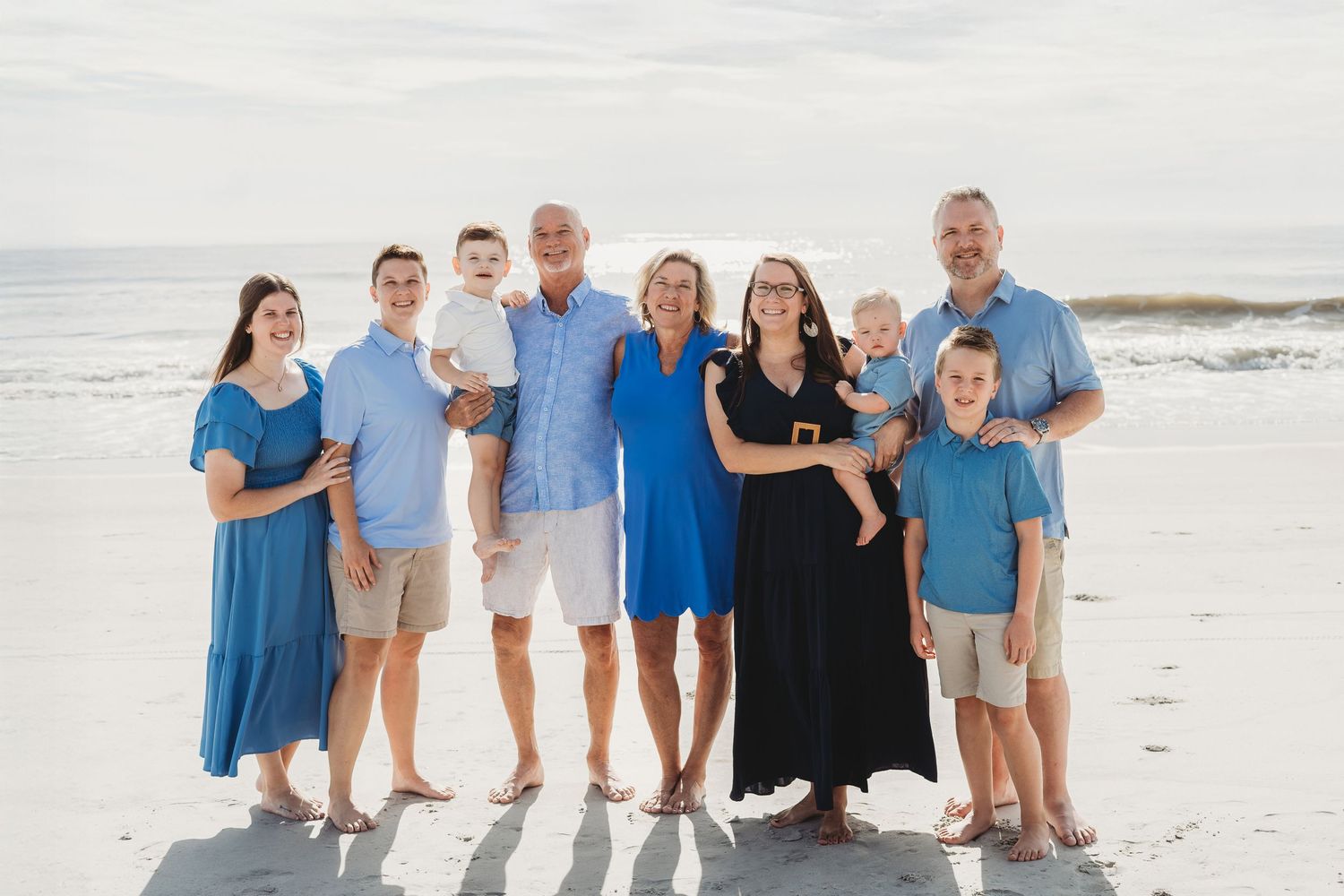 Family group wearing coordinated blue and white outfits posing together on a sunny beach.