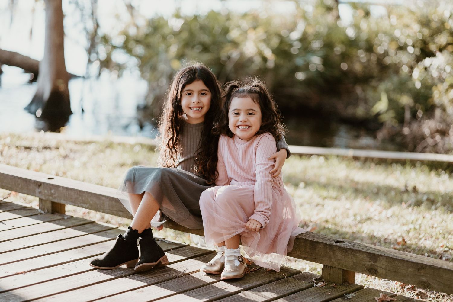 Two children sit together on a wooden deck in casual outfits on a sunny day.