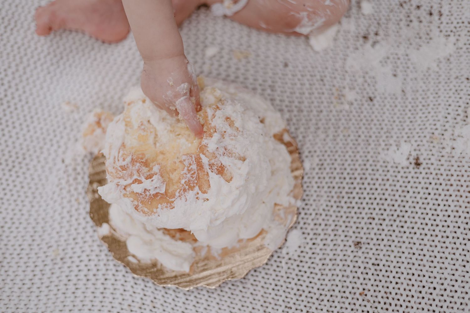 Tiny hands smash into a white frosted dessert on a gray background.