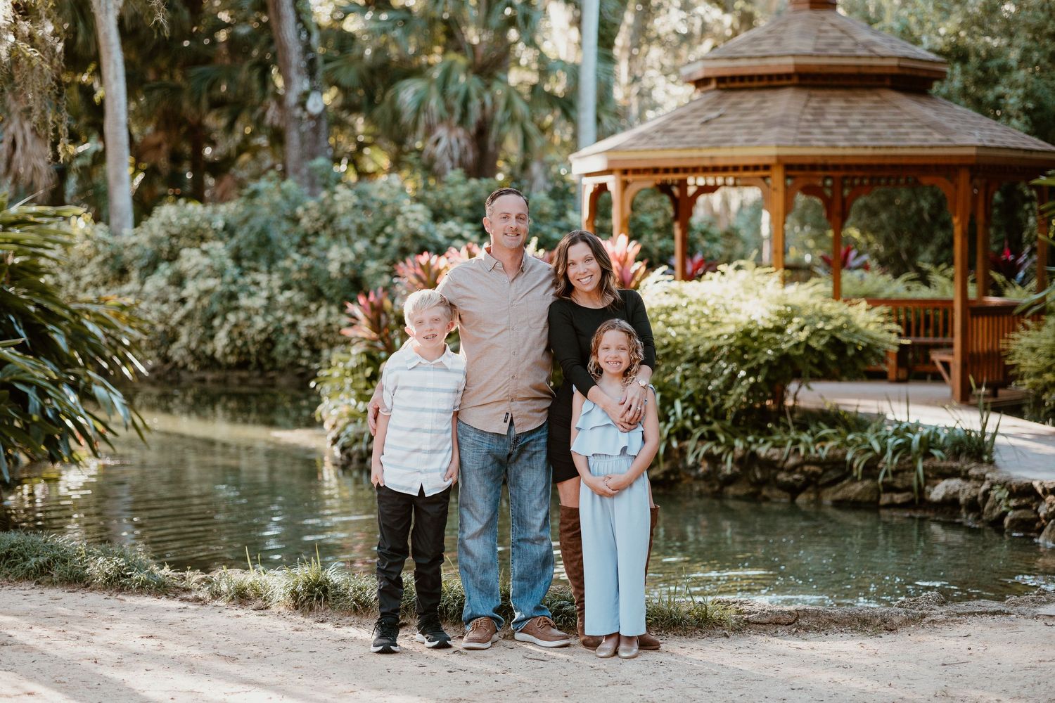 A group of people walking together through a lush garden setting with gazebos and tropical landscaping.