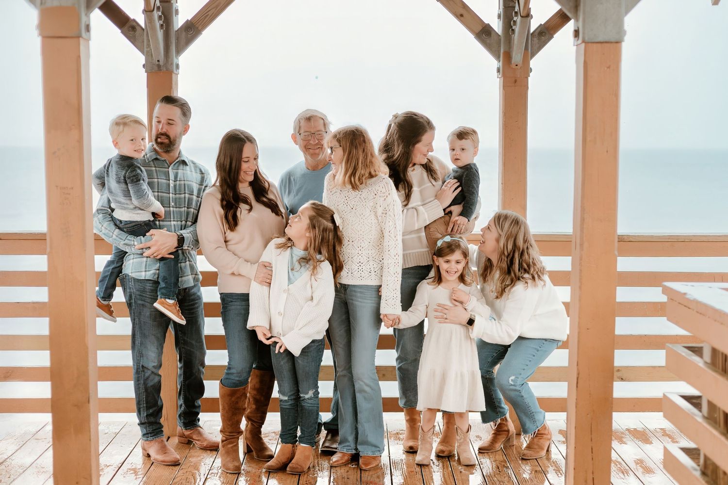 A group sits together on a wooden deck overlooking the ocean, dressed casually in light colors and denim.