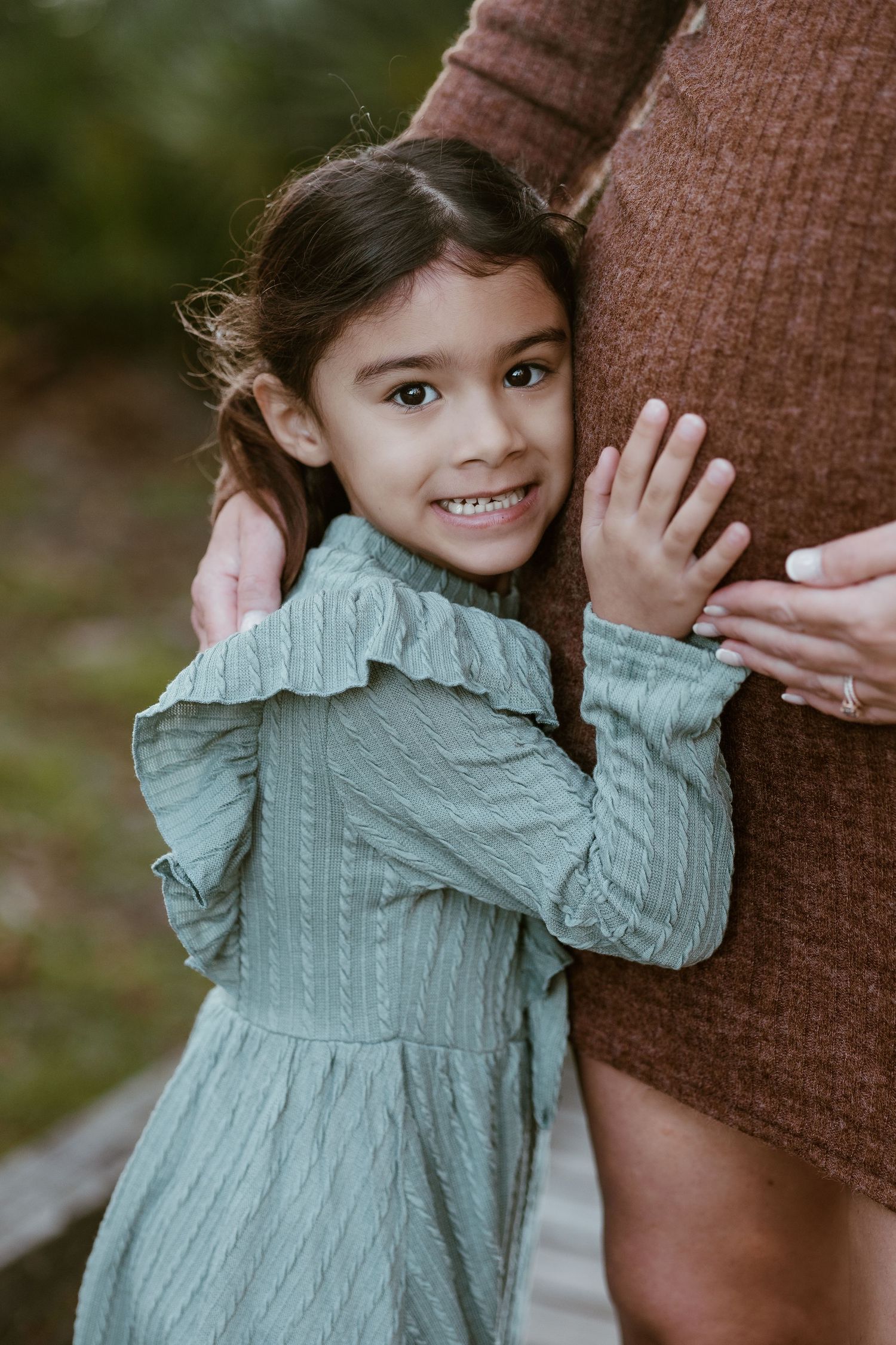 Child in mint green dress poses playfully against brown textured background.