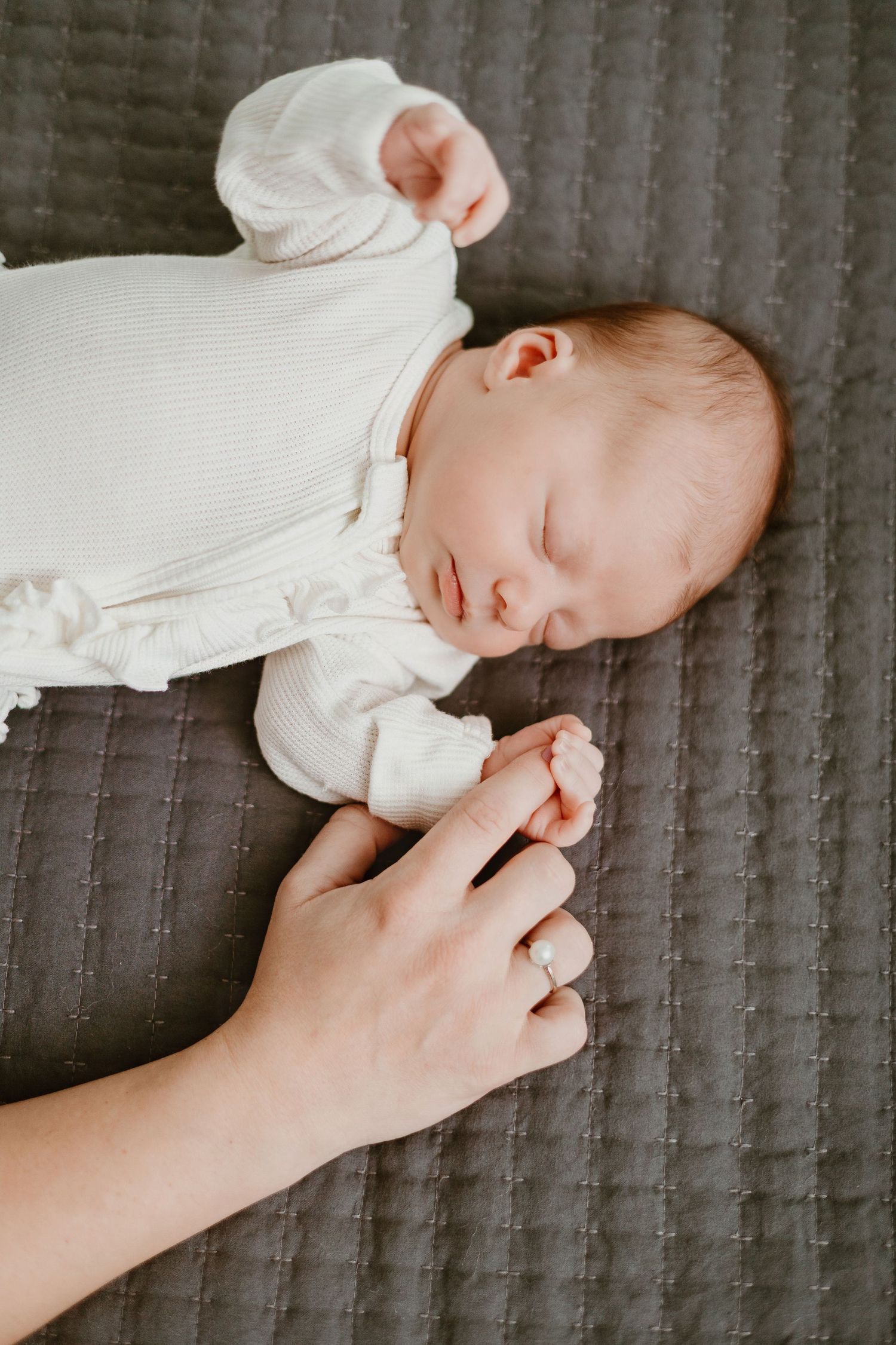 Sleeping infant in white clothing on a textured gray surface.