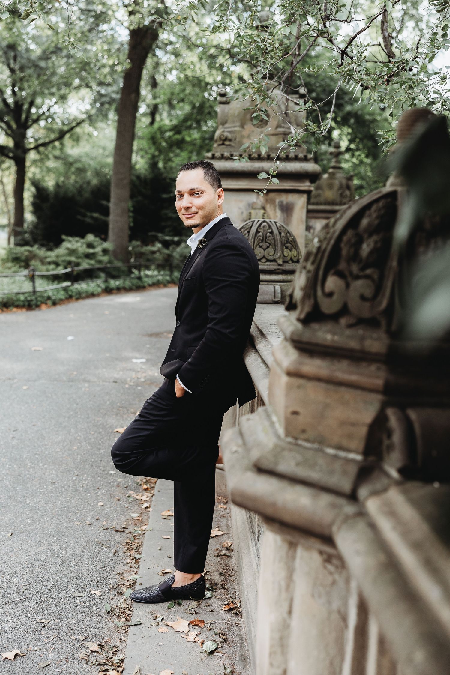 Professional photoshoot in an outdoor park setting with decorative stone architecture.