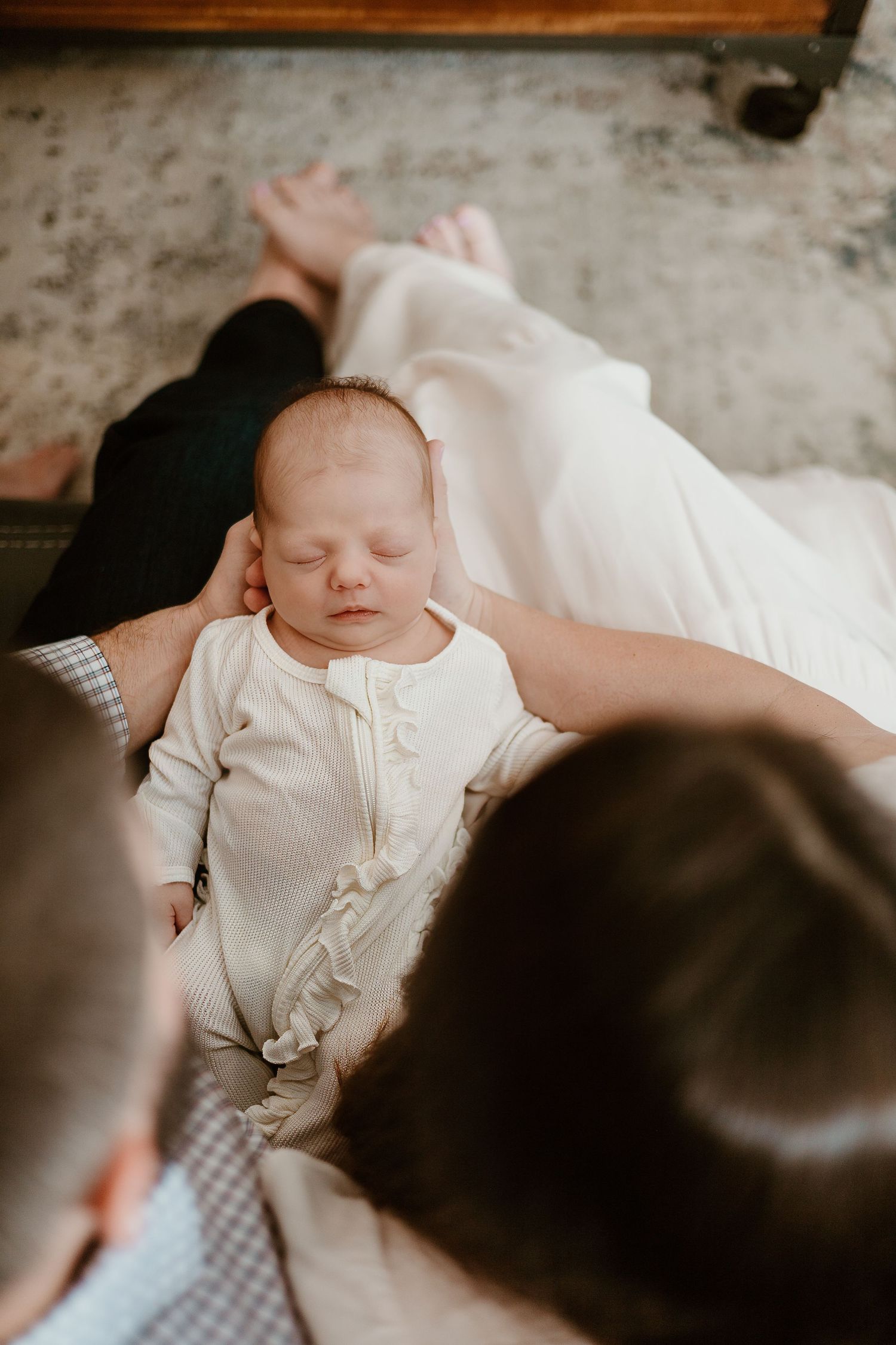 A sleeping infant in white clothing is surrounded by caring adults.