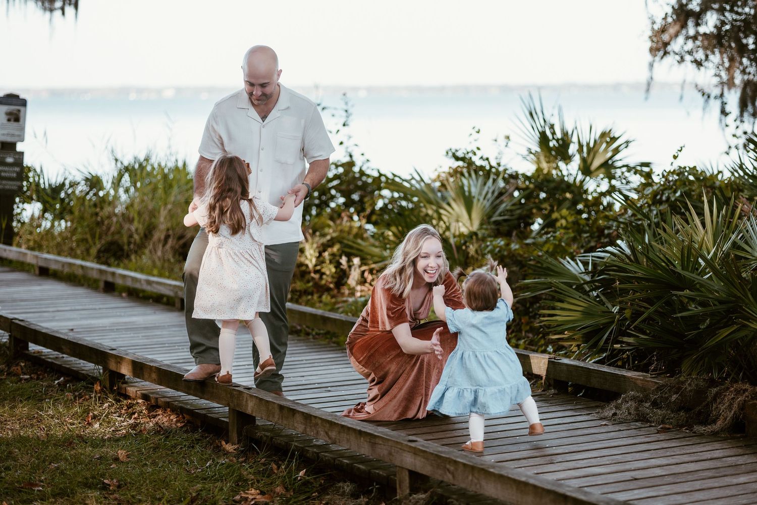 A family spends time together on a wooden boardwalk near the water at sunset.