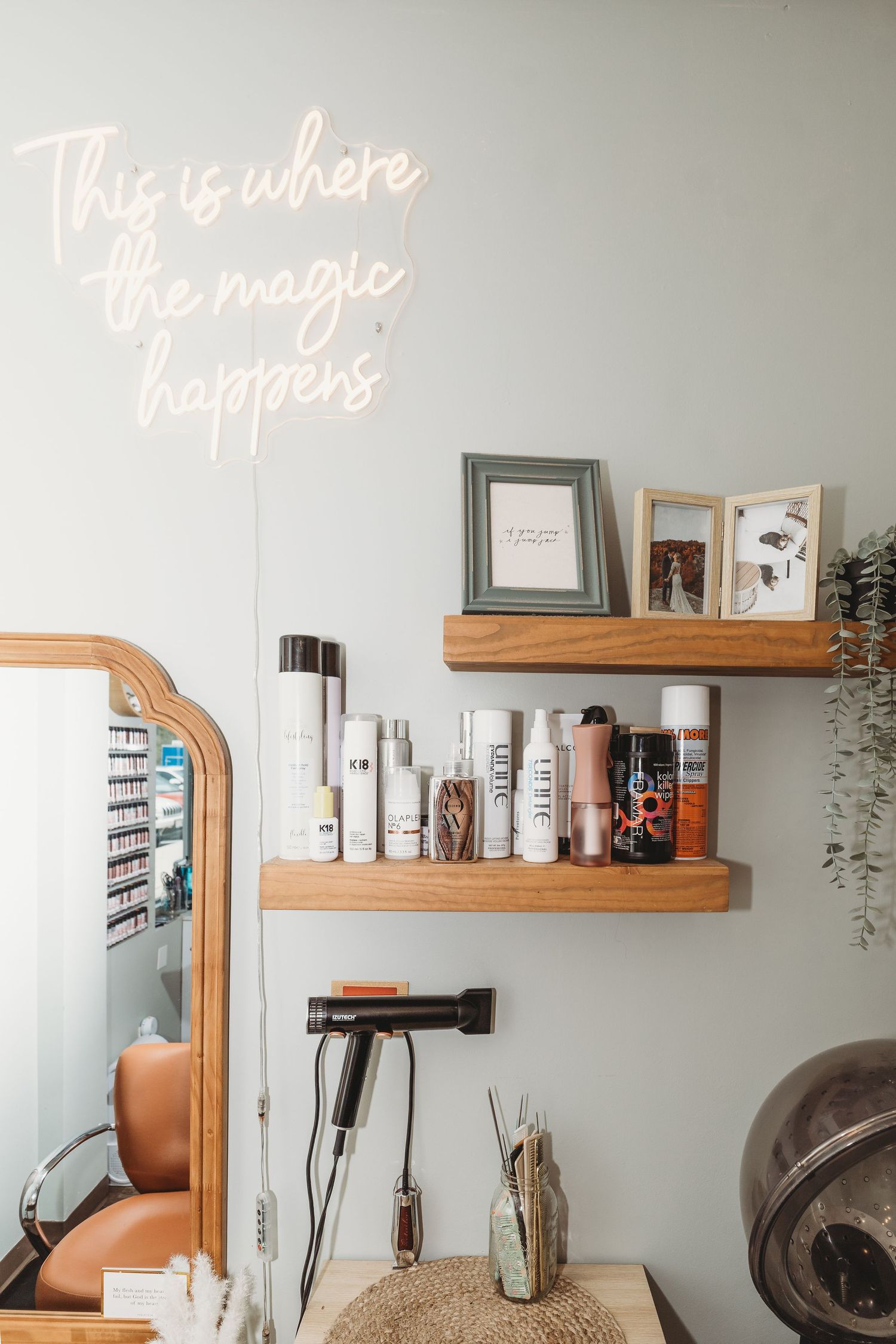 Salon wall with neon sign reading 'this is where the magic happens' and wooden floating shelves.