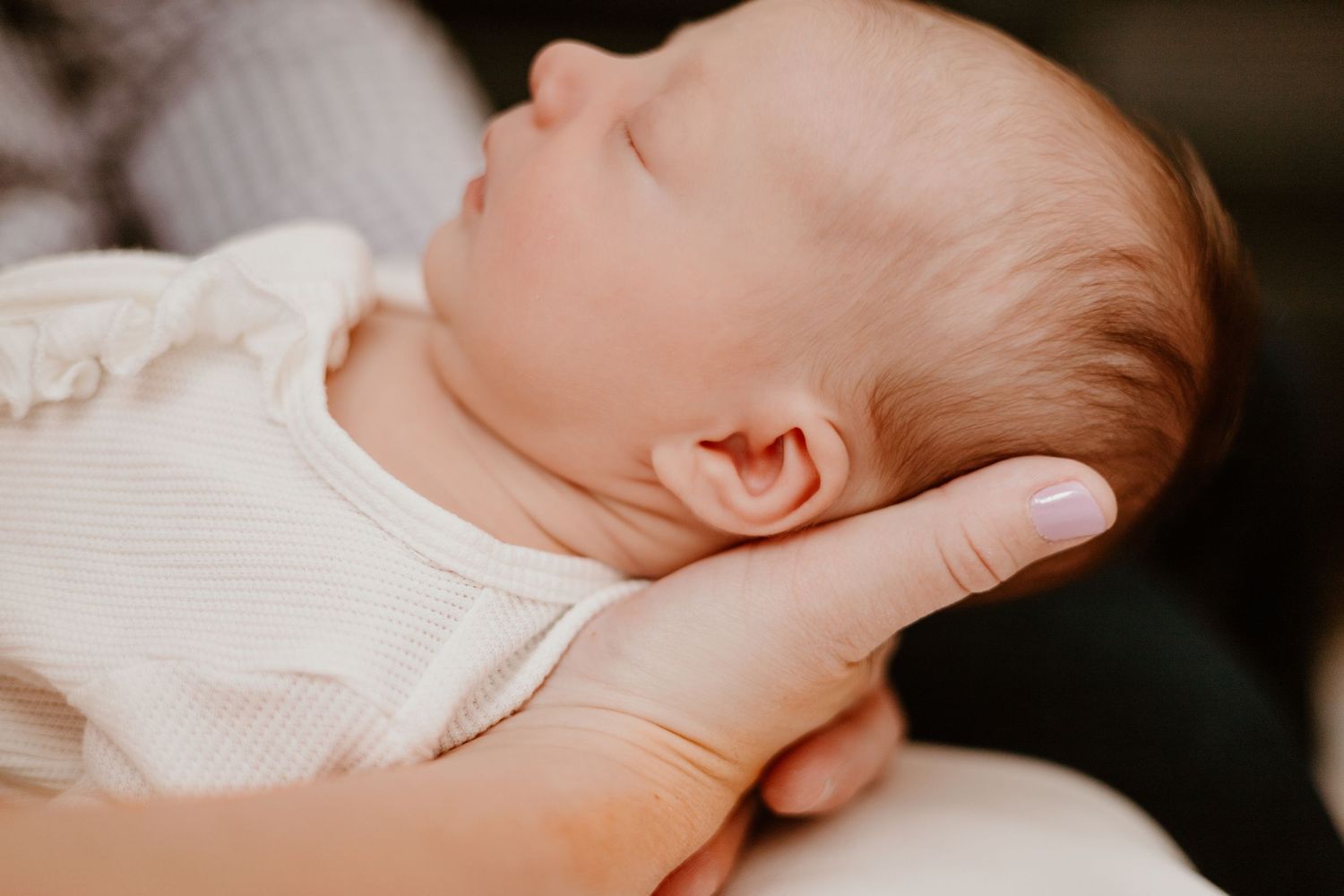 A peaceful newborn baby sleeps soundly while being held in gentle hands.