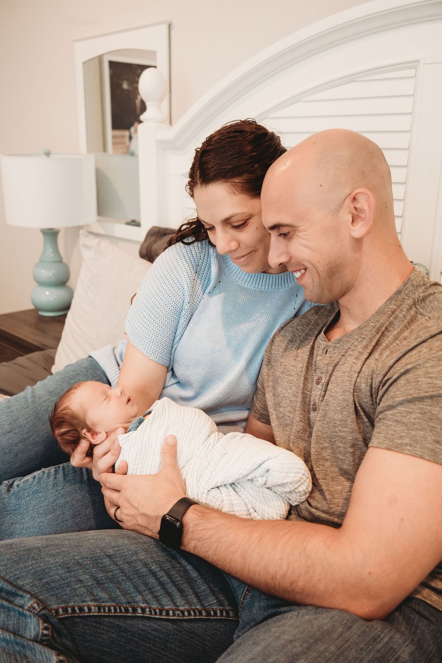Family snuggling together on a blue couch while holding a newborn baby.