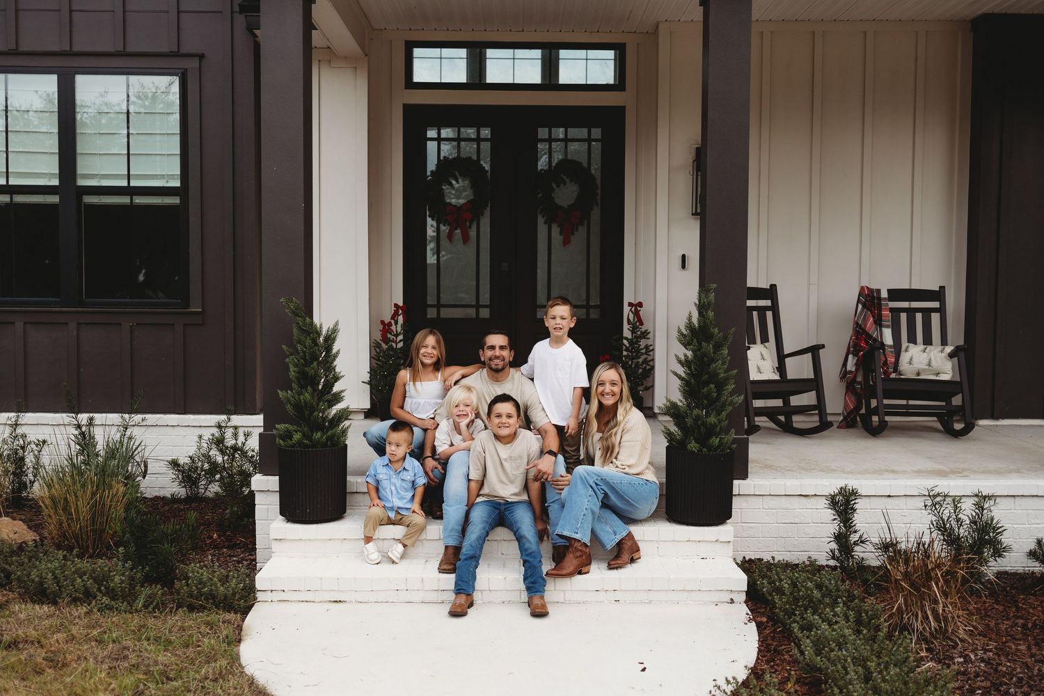 Family sits together on white porch steps of craftsman style home for outdoor photo session.