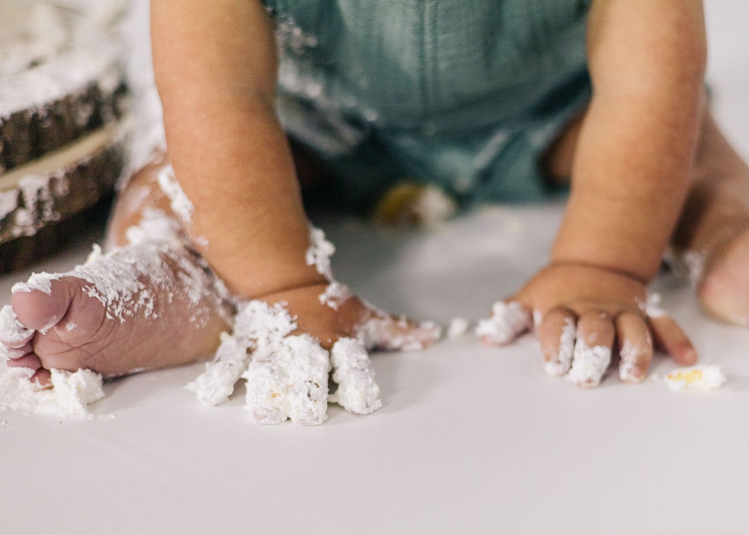 Close up of tiny hands covered in white cake frosting on wooden surface.