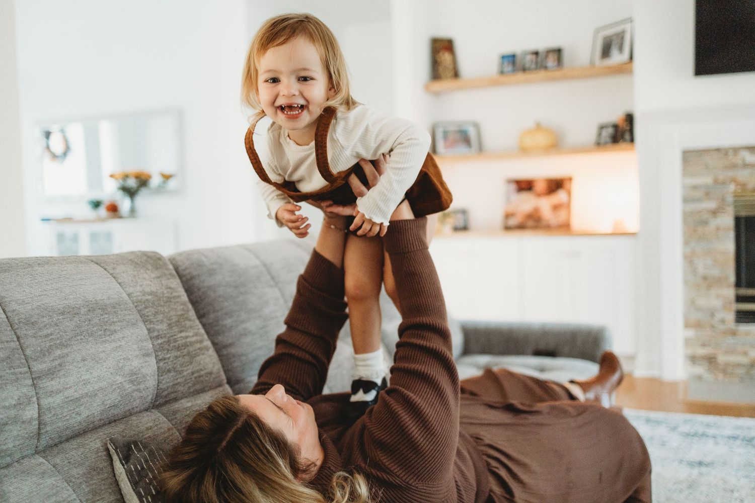 A playful moment captured in a bright living room with a grey couch and floating shelves on the wall.