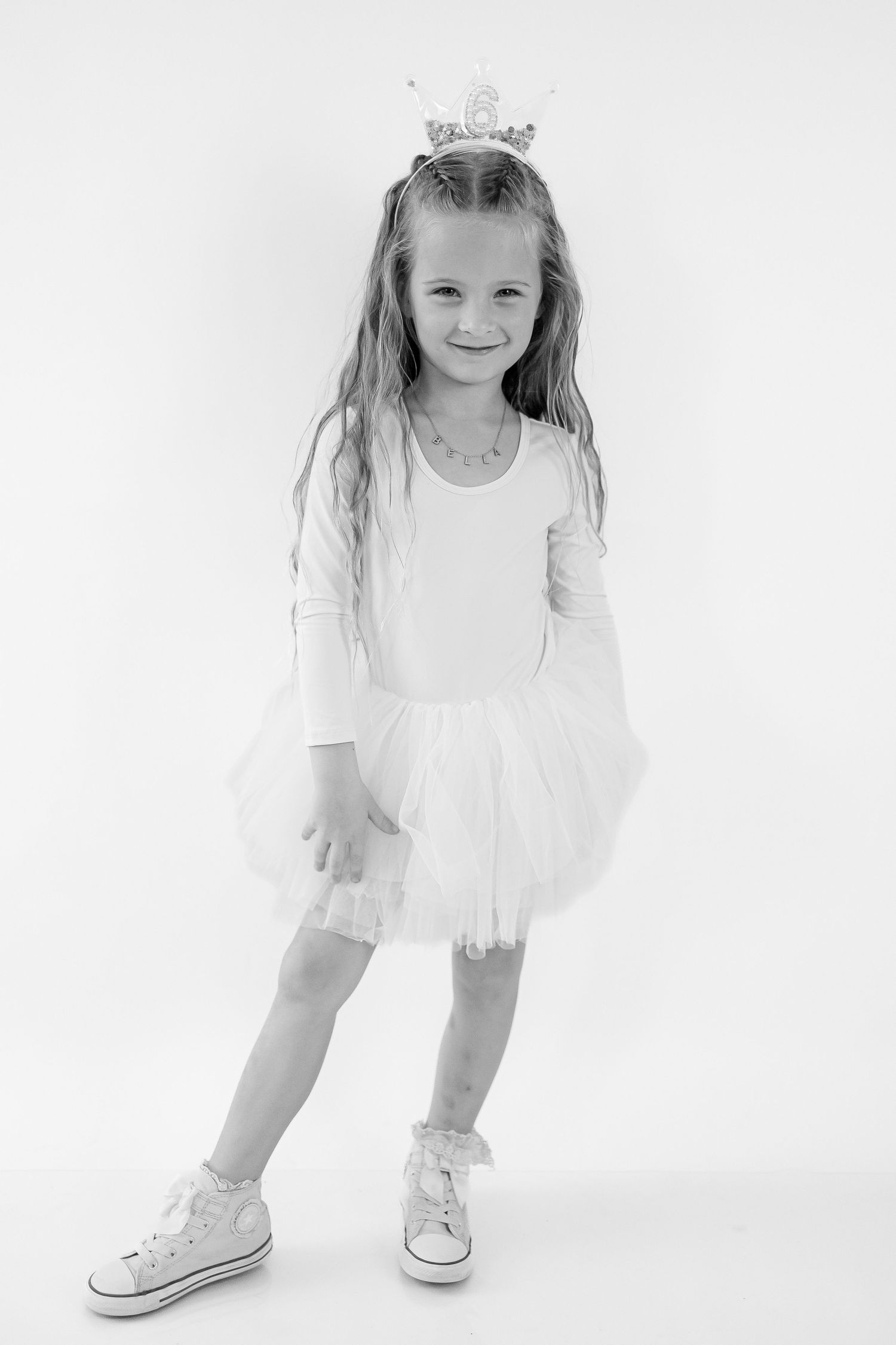 A young child in a white dress and tiara poses gracefully in three artistic black and white portraits.