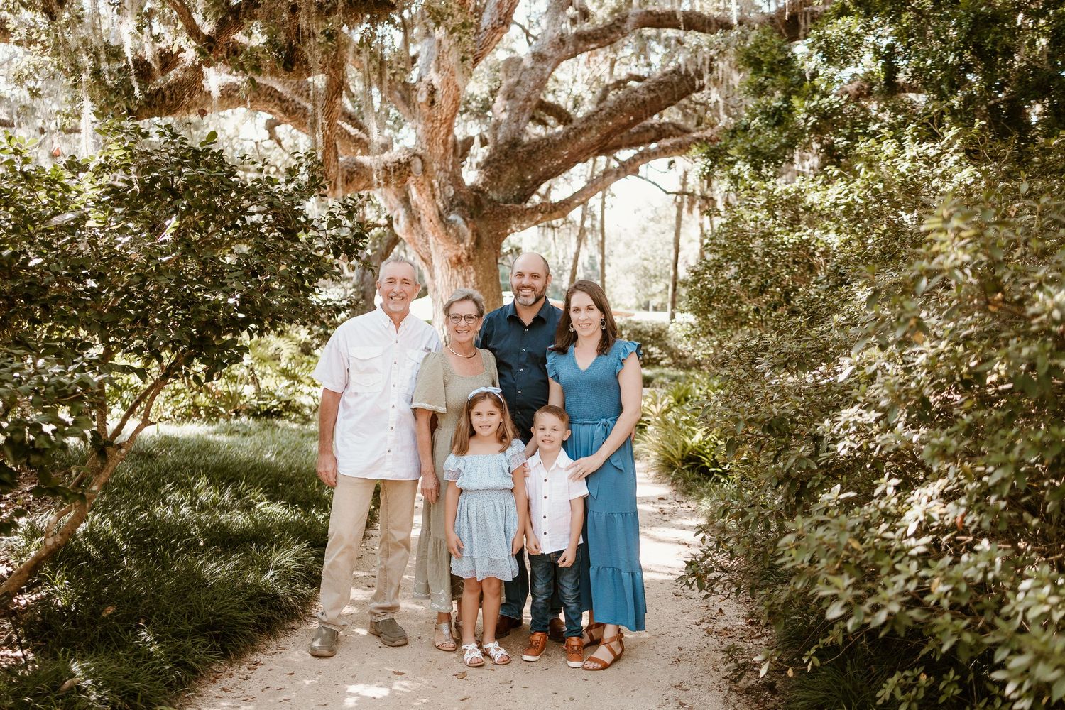 A group in coordinated blue and white outfits poses together for outdoor portraits under shady trees.
