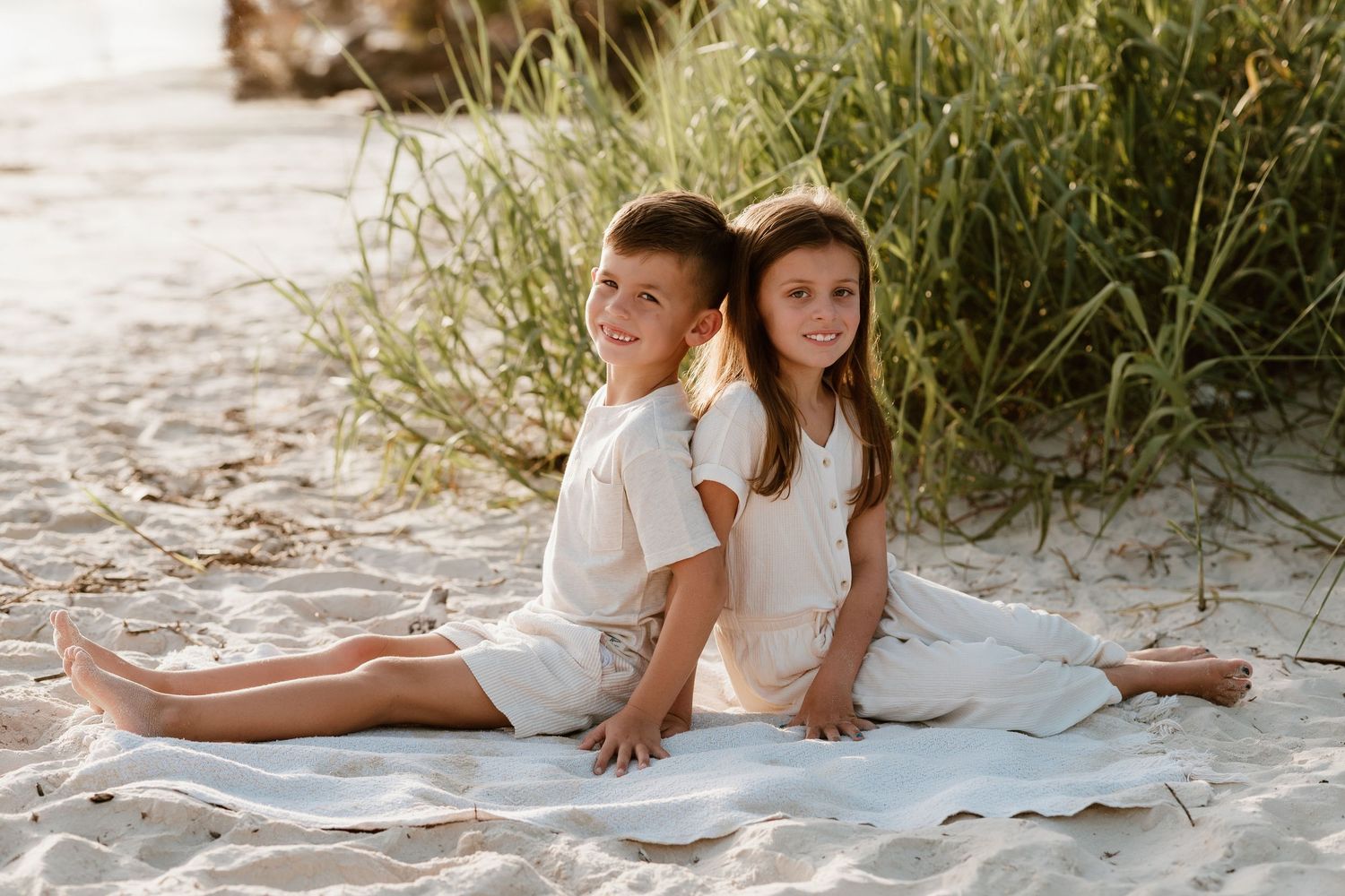 Two children sitting back to back on blanket at beach.