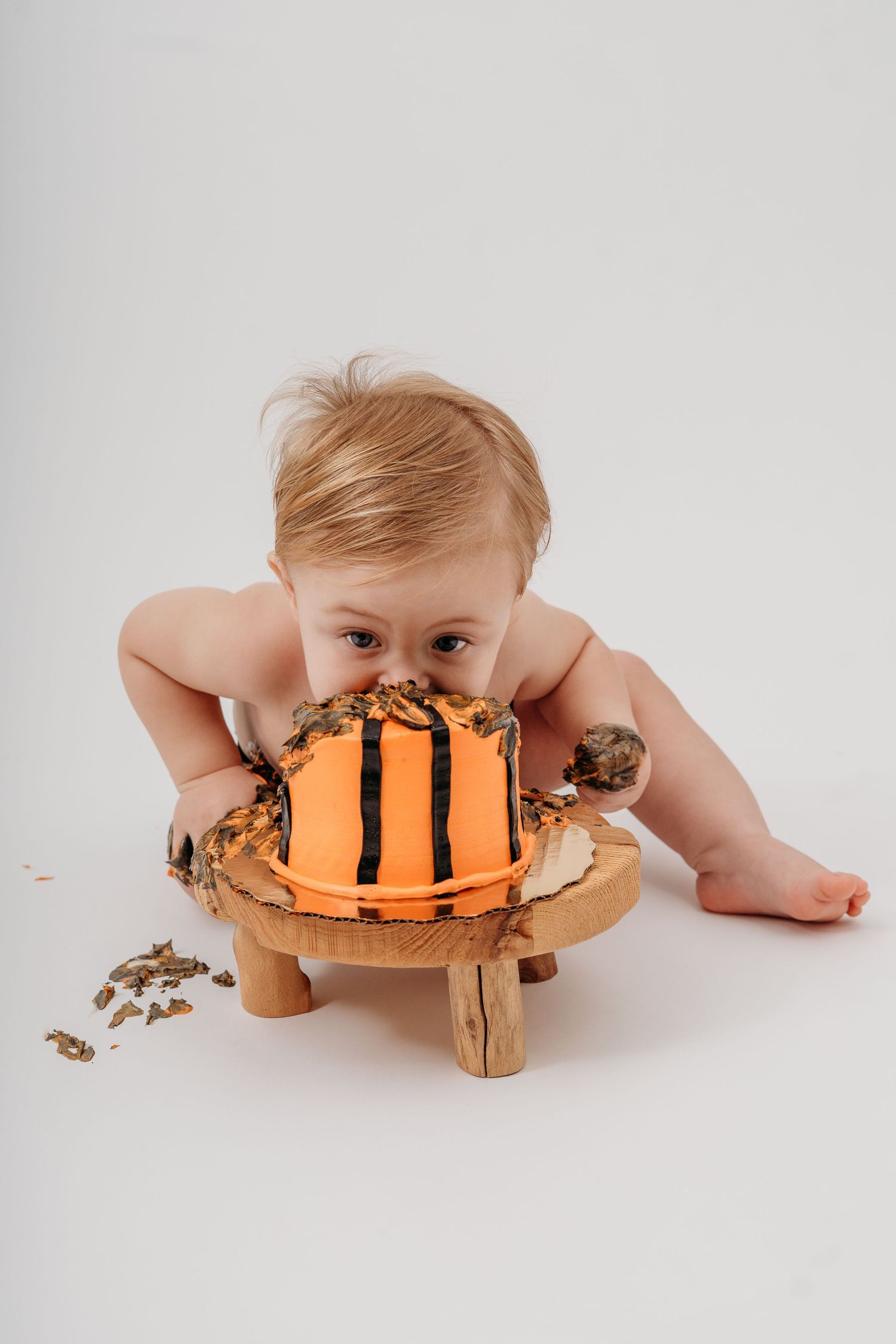 Baby enthusiastically destroying basketball-themed cake on wooden surface.