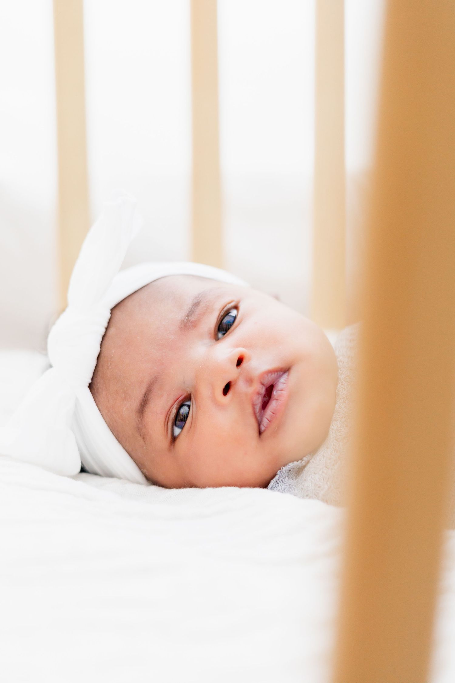 View through crib slats of baby lying in white bedding.