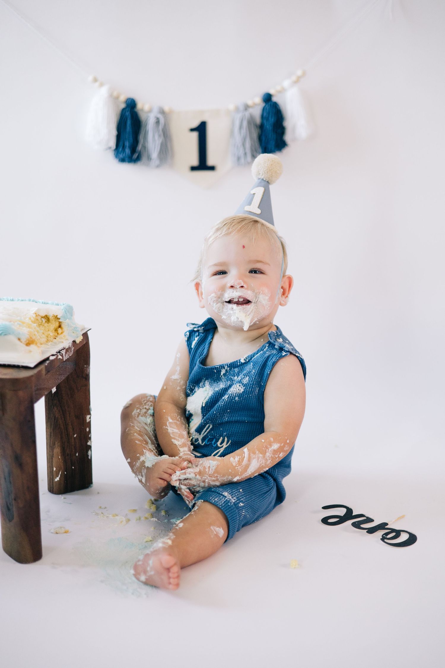 First birthday cake smash session with baby in navy blue outfit getting messy with dessert.