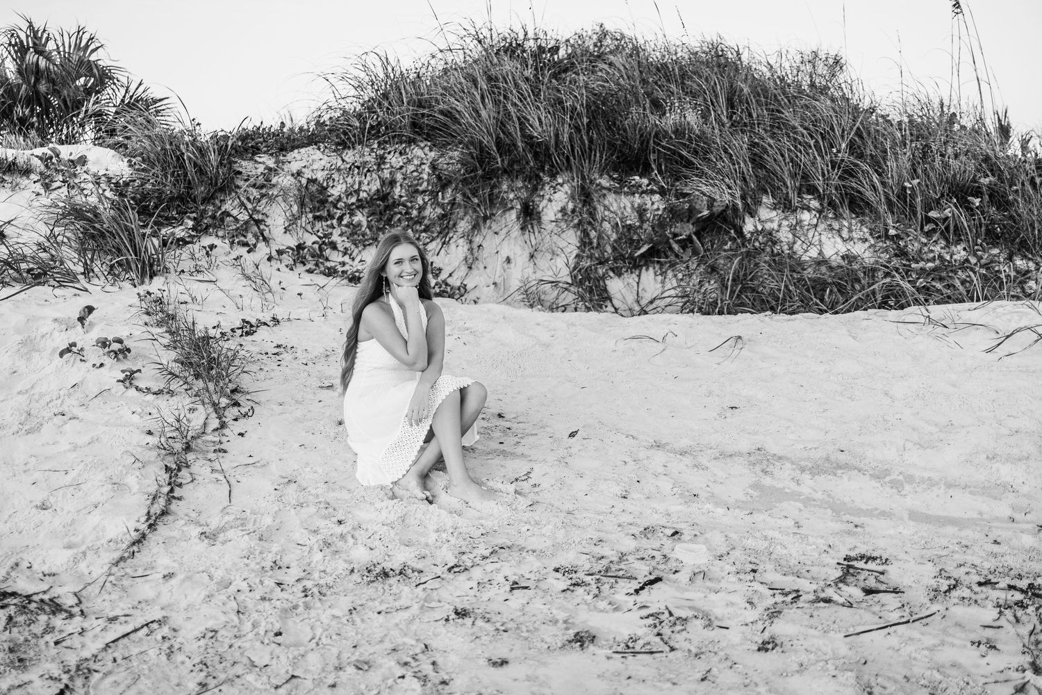 Black and white panoramic view of sand dunes with scattered vegetation against a cloudy sky.