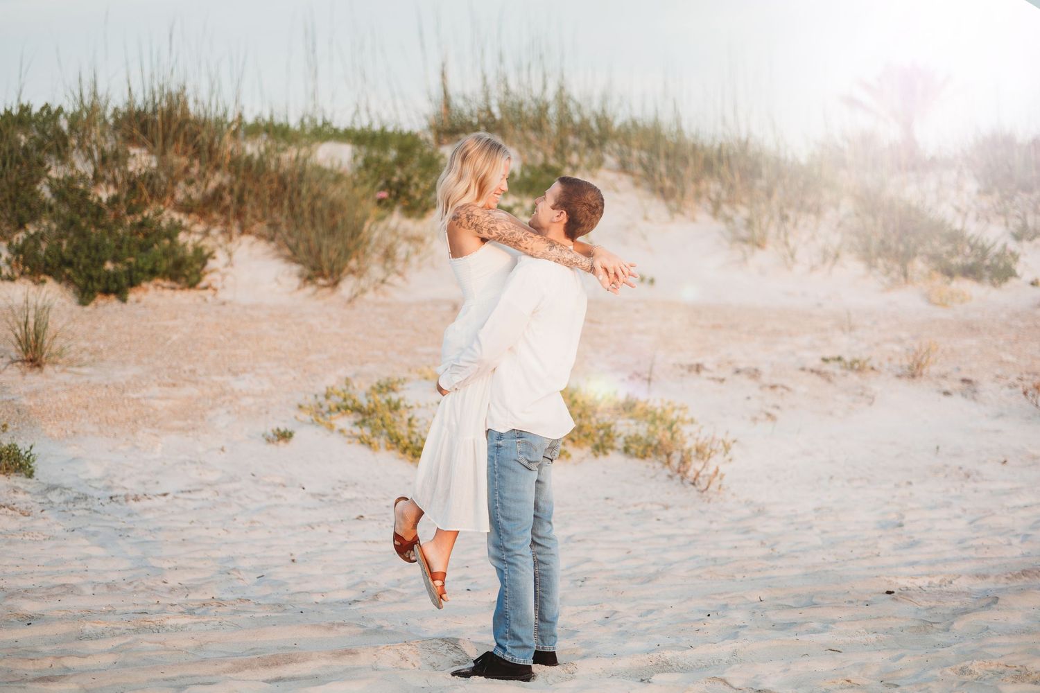 A couple shares a playful moment together on a sandy beach at sunset.