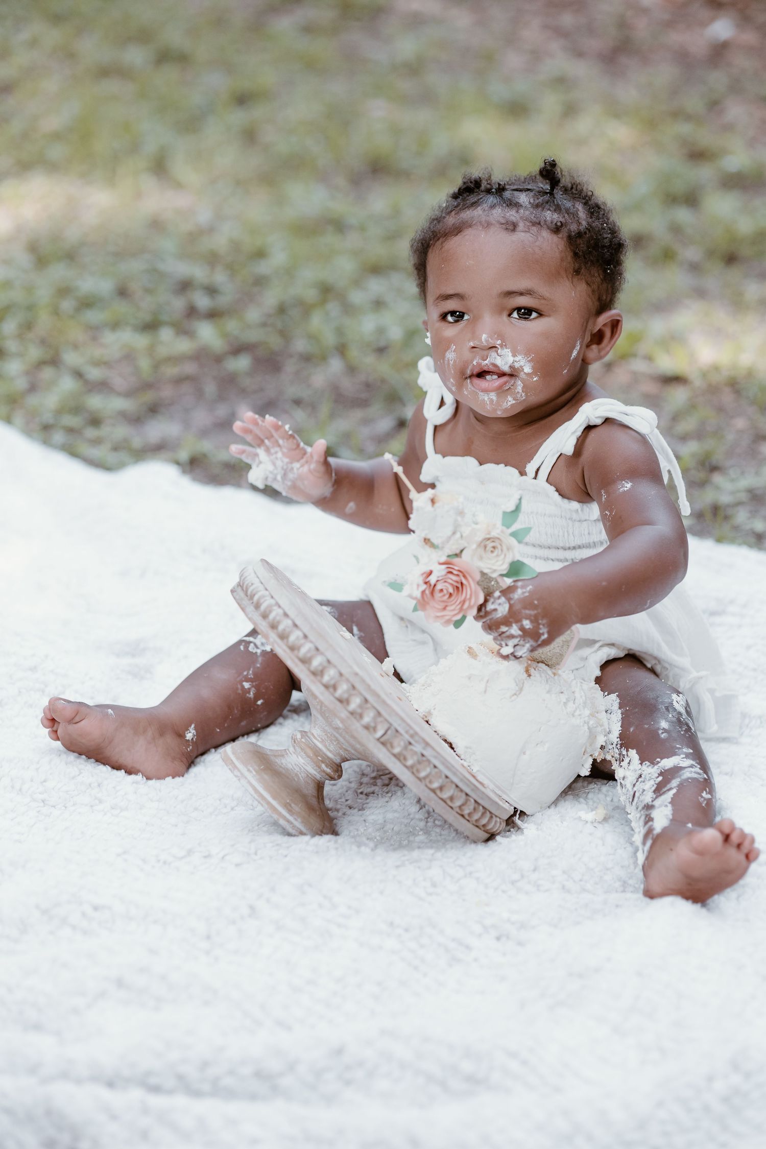 Baby in white dress plays with cake during professional cake smash photo session.